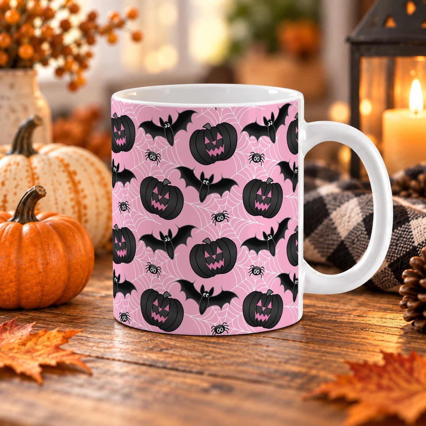 White 11 oz ceramic Halloween mug with black jack-o'-lanterns, bats, spiders, and white spider webs on a pink background, sitting upon a wooden table with fall decor around it.