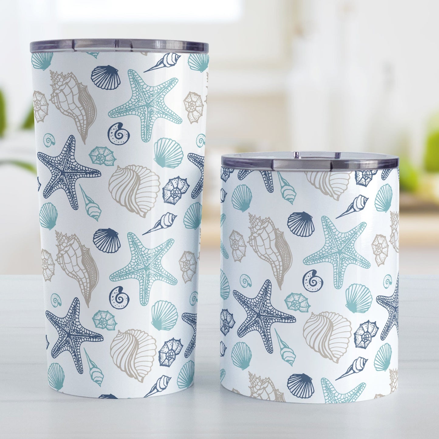 Coastal Seashells Pattern Tumbler Cup (20oz or 10oz) at Amy's Coffee Mugs. A stainless steel tumbler cup with a summer beach-inspired pattern of seashells in navy blue, teal, and sandy beige over white that wraps around the cup. Image shows both sized cups on a table next to each other.