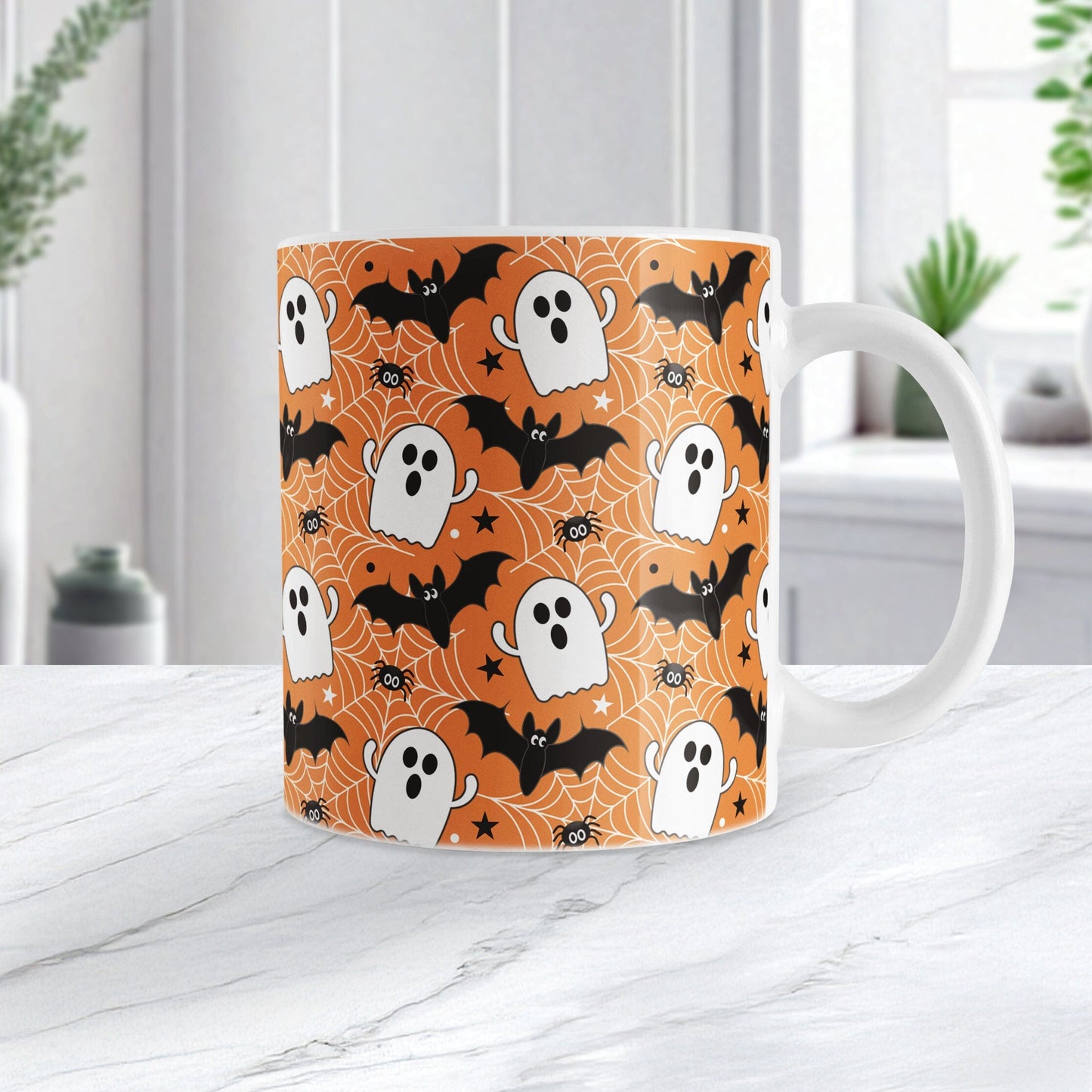 Halloween-themed mug with ghost, bat, and spider pattern on an orange background. Photo shows the mug on a marble tabletop.