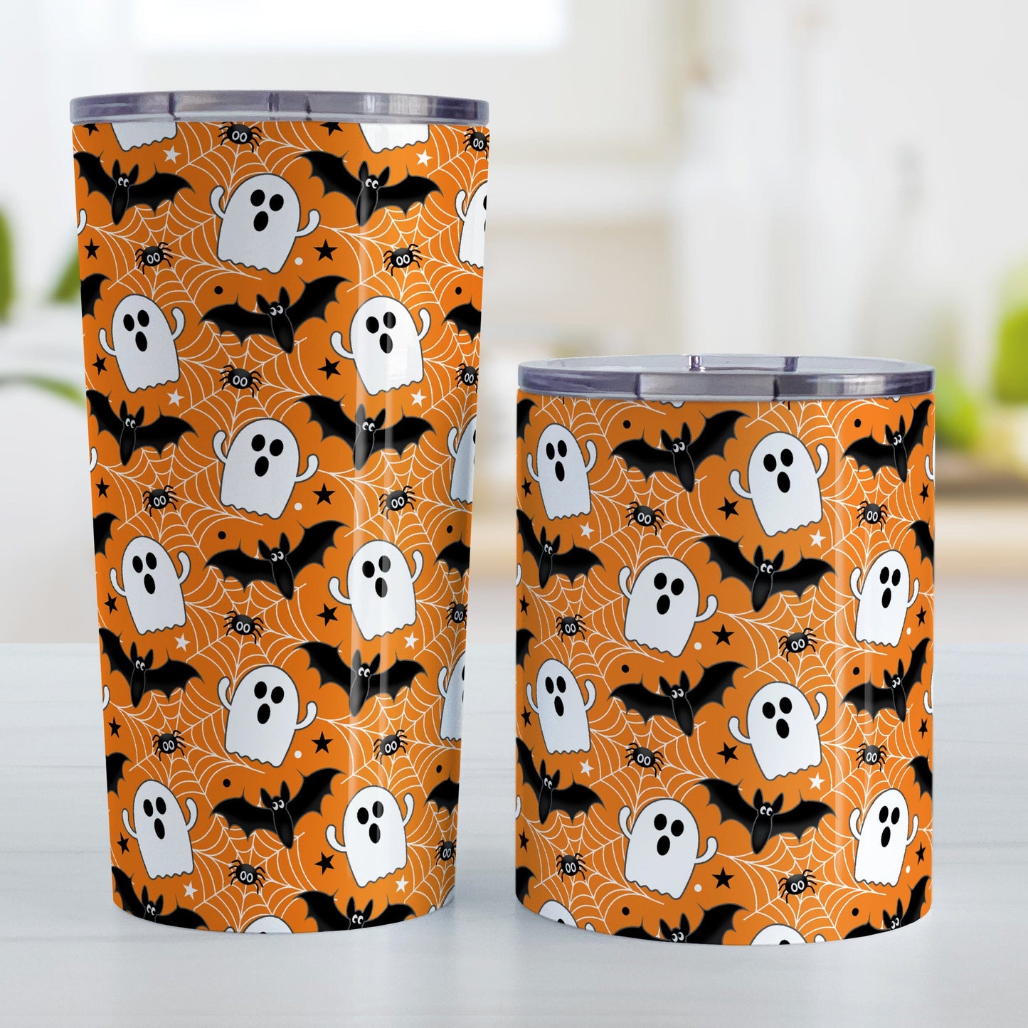 Two Halloween-themed tumblers with ghost, bat, and spider web pattern on an orange background.
