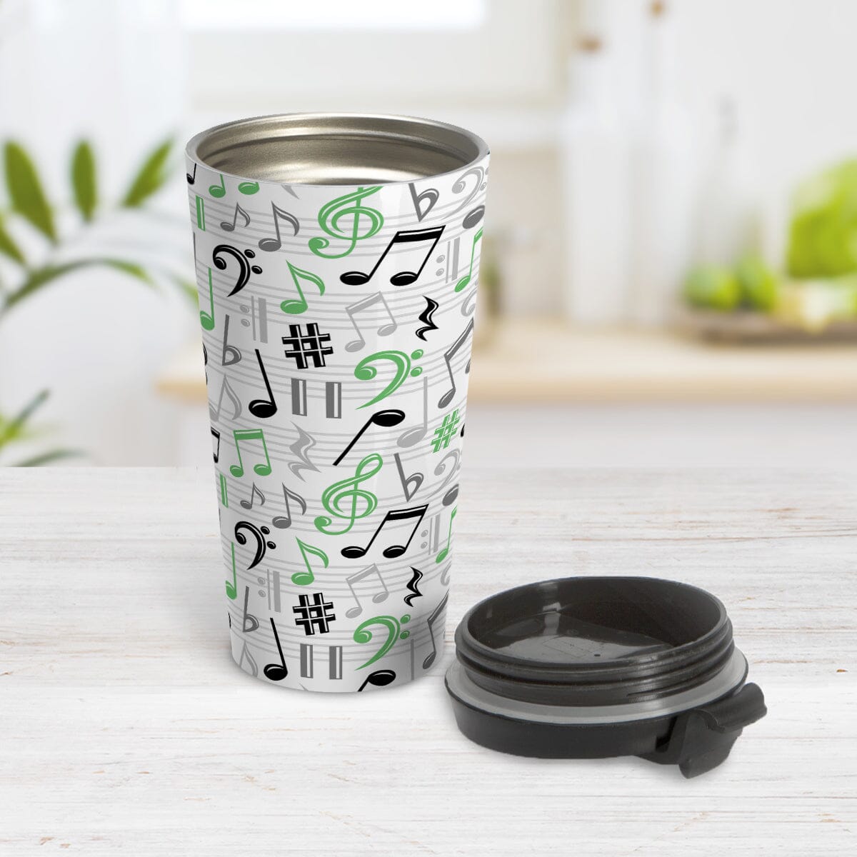 Green Music Notes Pattern Travel Mug (15oz) at Amy's Coffee Mugs. A stainless steel travel mug designed with music notes and symbols in green, black, and gray in a pattern that wraps around the travel mug. Image shows the travel mug open with the lid laying on the tabletop beside it.