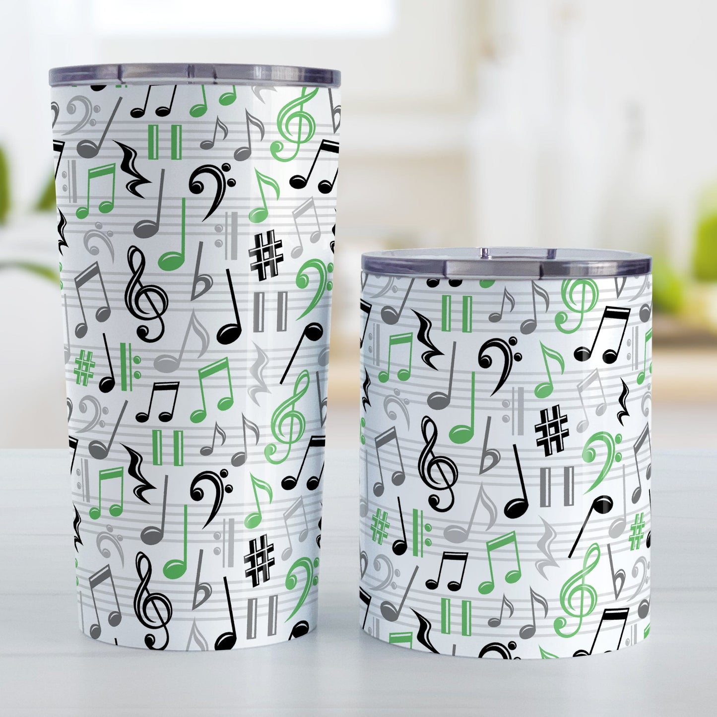 Green Music Notes Pattern Tumbler Cups (20oz or 10oz) at Amy's Coffee Mugs. Stainless steel tumbler cups designed with music notes and symbols in green, black, and gray in a pattern that wraps around the cups. Photo shows both sized cups on a table next to each other.