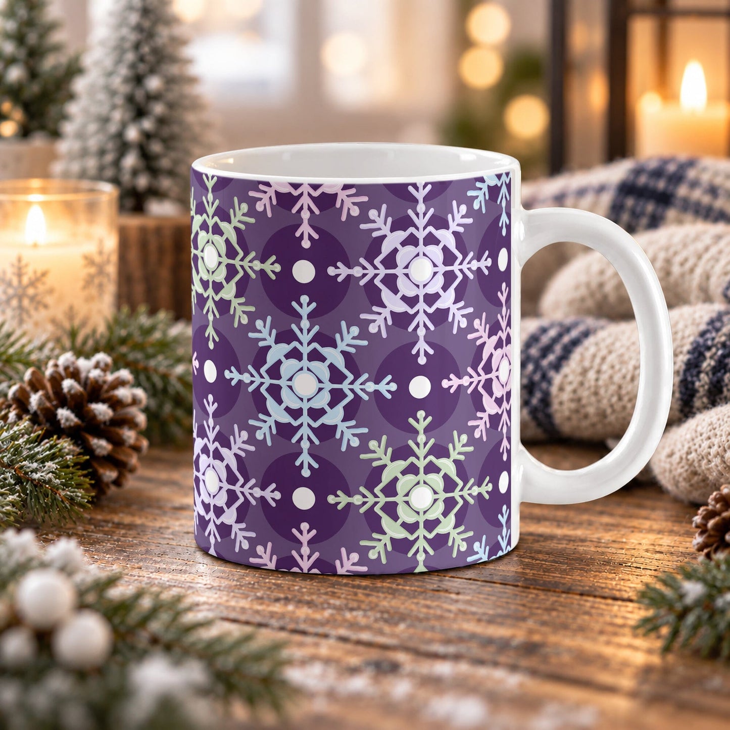 11 oz pastel snowflake mug with pink, blue, green, and lavender snowflakes over a deep purple for a geometric winter pattern, on a wooden table with winter decor around it including pine cones, pine boughs, candles, and a cozy plaid blanket.