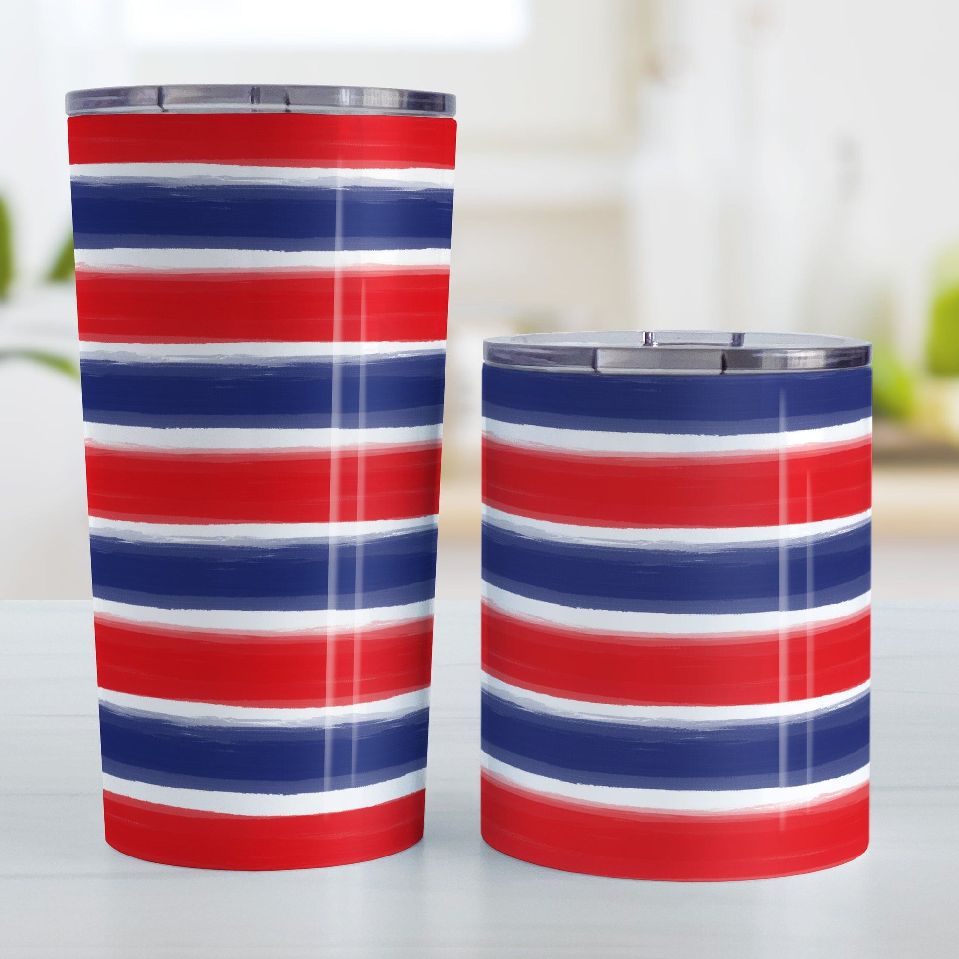 Patriotic Paint Brush Strokes Tumbler Cup (20oz or 10oz) at Amy's Coffee Mugs. A stainless steel tumbler cup featuring a print of artistic paint brush strokes horizontally across the tumbler cup, in alternating colors of red and blue over white to celebrate the 4th of July (Independence Day) holiday. Image shows both sized cups on a table next to each other.