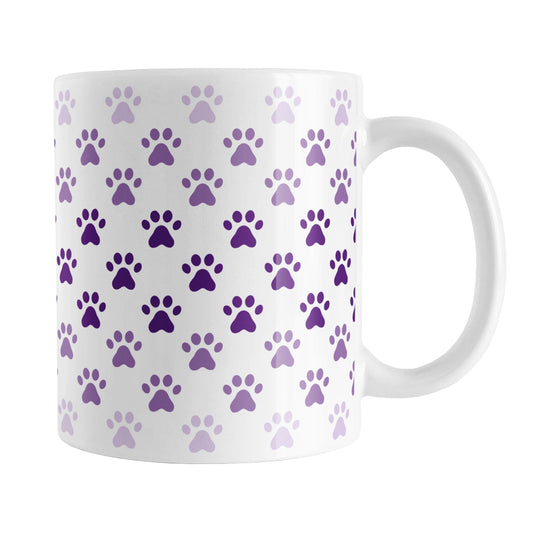 Paw Prints in Purple Mug (11oz) at Amy's Coffee Mugs. A ceramic coffee mug designed with paw prints in different shades of purple, with the darker purple color across the middle and the lighter purple along the top and bottom, in a pattern that wraps around the mug to the handle.