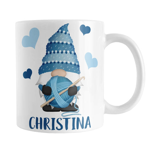 Personalized Blue Crochet Gnome Mug (11oz) at Amy's Coffee Mugs. A ceramic coffee mug designed with a cute gnome wearing a blue crochet hat while holding a ball of blue yarn and a crochet hook with blue hearts around him. Your name is printed in a fun blue font below the gnome. This adorable illustration and personalization is on both sides of the mug.