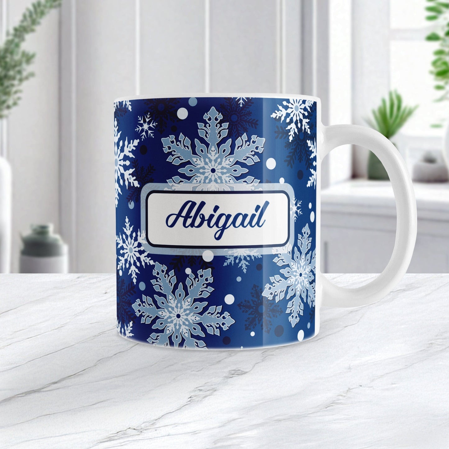 Personalized Classic Blue Snowflake Winter Mug (11oz) at Amy's Coffee Mugs. A ceramic coffee mug designed with a pattern of different shades of blue snowflakes over a classic blue background color that wraps around the mug to the handle. Your name is custom printed in a blue script font on both sides of the mug. Image shows the mug on a white marble countertop.