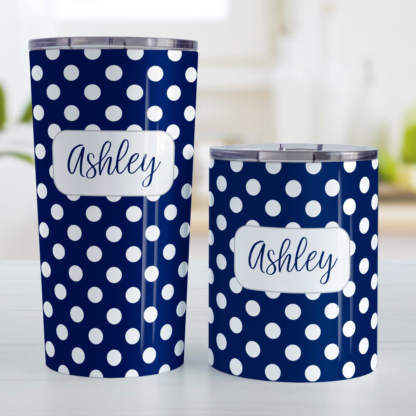 Personalized Dark Blue Polka Dot Tumbler Cup (20oz and 10oz, stainless steel insulated) at Amy's Coffee Mugs. These cups are designed with a pattern of white polka dots over a dark navy blue background color that wraps around the cups. Your name is personalized in a dark blue script font over the polka dot pattern. Photo shows both sized cups on a table next to each other.
