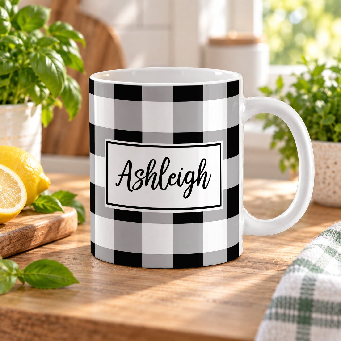 11 oz personalized black and white buffalo plaid mug with custom name in a white framed area, sitting on a wooden table in a bright kitchen with green plants, a tea towel, and lemons on a wood cutting board.