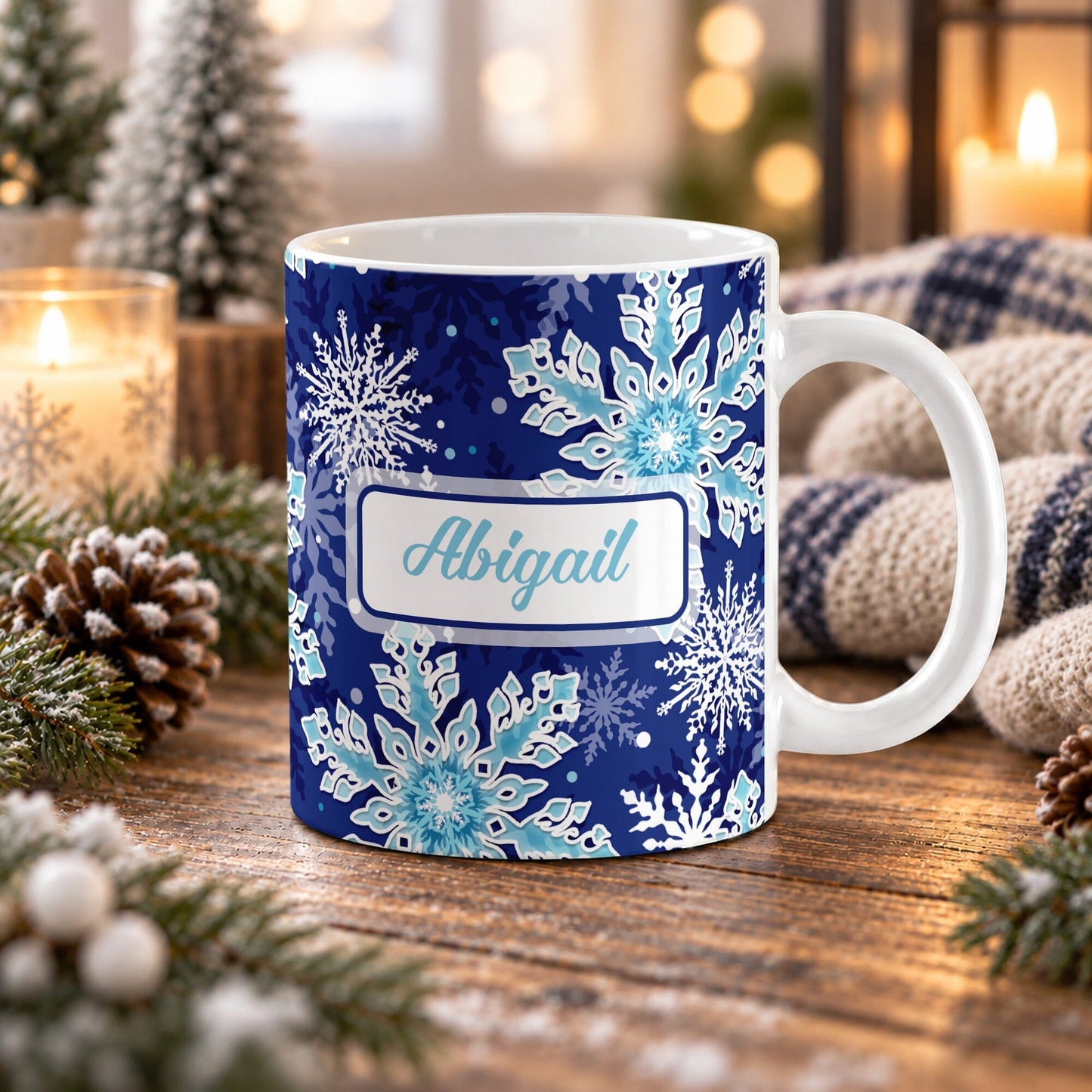 11 oz personalized snowflake mug with navy blue and aqua winter pattern and custom aqua script name in a white rectangular area on both sides, shown on a wooden table with winter decor around it.