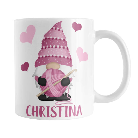 Personalized Pink Crochet Gnome Mug (11oz) at Amy's Coffee Mugs. A ceramic coffee mug designed with a cute gnome wearing a pink crochet hat while holding a ball of pink yarn and a crochet hook with pink hearts around him. Your name is printed in a fun pink font below the gnome. This adorable illustration and personalization is on both sides of the mug.
