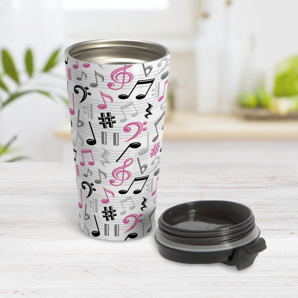 Pink Music Notes Pattern Travel Mug (15oz) at Amy's Coffee Mugs. A stainless steel travel mug designed with music notes and symbols in pink, black, and gray in a pattern that wraps around the travel mug. Photo shows the travel mug open on a table with the lid laying beside it.