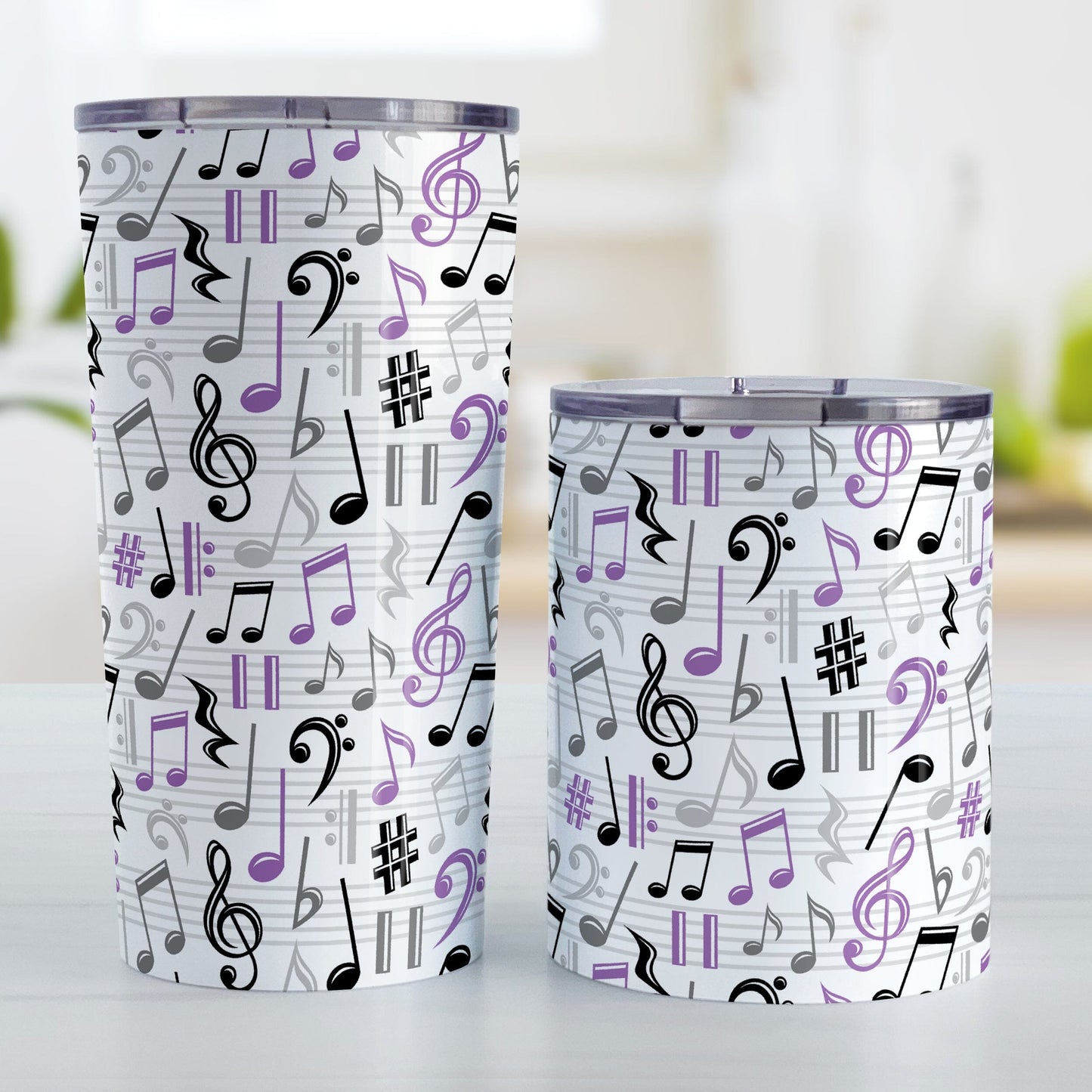 Purple Music Notes Pattern Tumbler Cups (20oz or 10oz) at Amy's Coffee Mugs. Stainless steel tumbler cups designed with music notes and symbols in purple, black, and gray in a pattern that wraps around the cups. Photo shows both sized cups on a table next to each other.