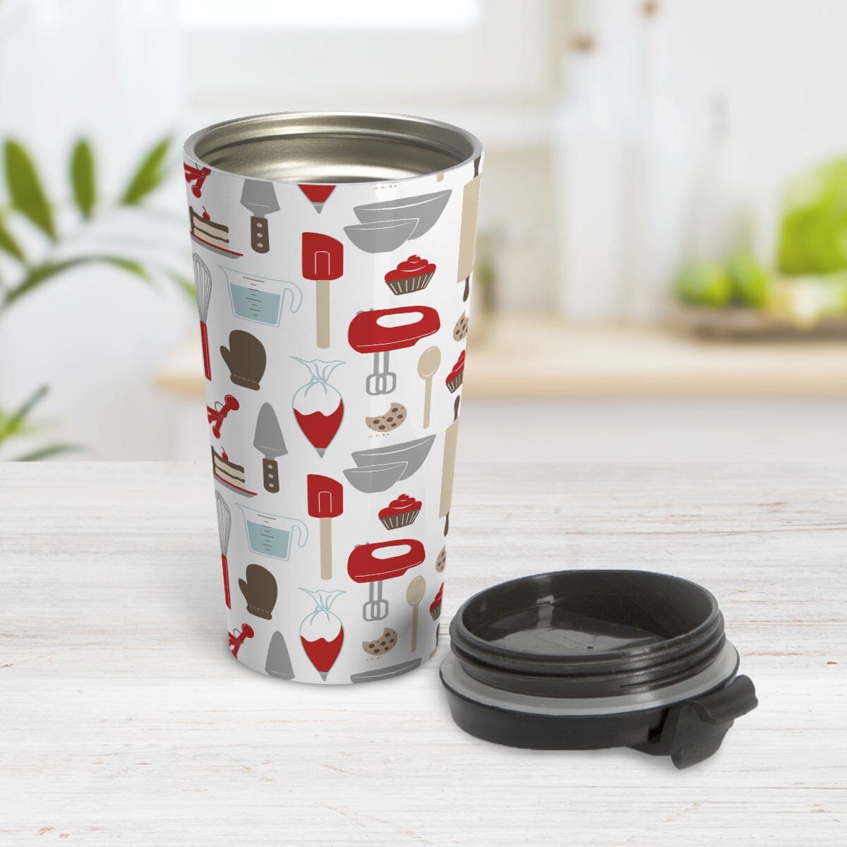 Red Baking Pattern Travel Mug (15oz) at Amy's Coffee Mugs. A stainless steel travel mug designed with a pattern of baking tools like spatulas, whisks, mixers, bowls, and spoons, with cookies, cupcakes, and cake all in a red, gray, brown, and beige color scheme that wraps around the travel mug. Photo shows the travel mug open with the lid on the tabletop next to it.