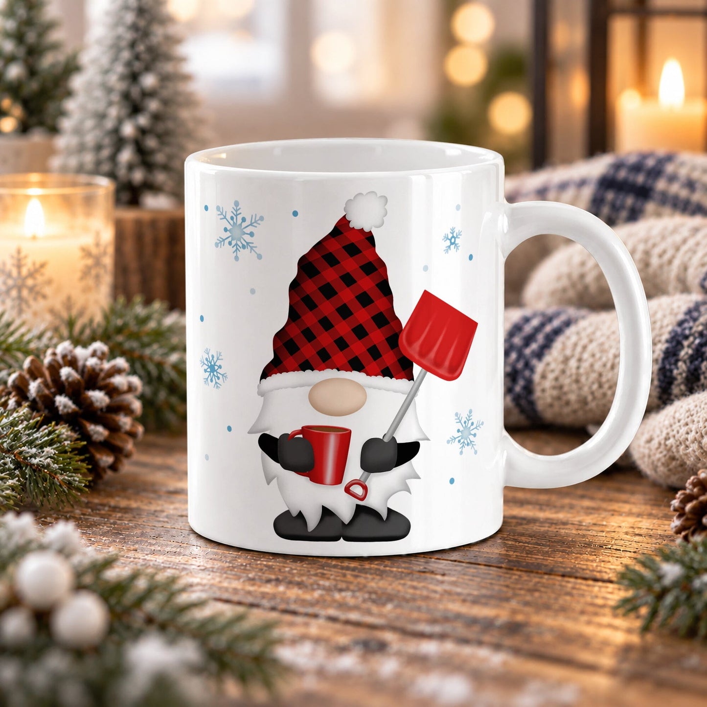 An 11 oz white ceramic mug featuring a festive holiday winter gnome design with a red and black buffalo plaid hat, white beard, black shoes, and a red snow shovel, set on a wooden table surrounded by candles, pinecones, and a cozy knit blanket.