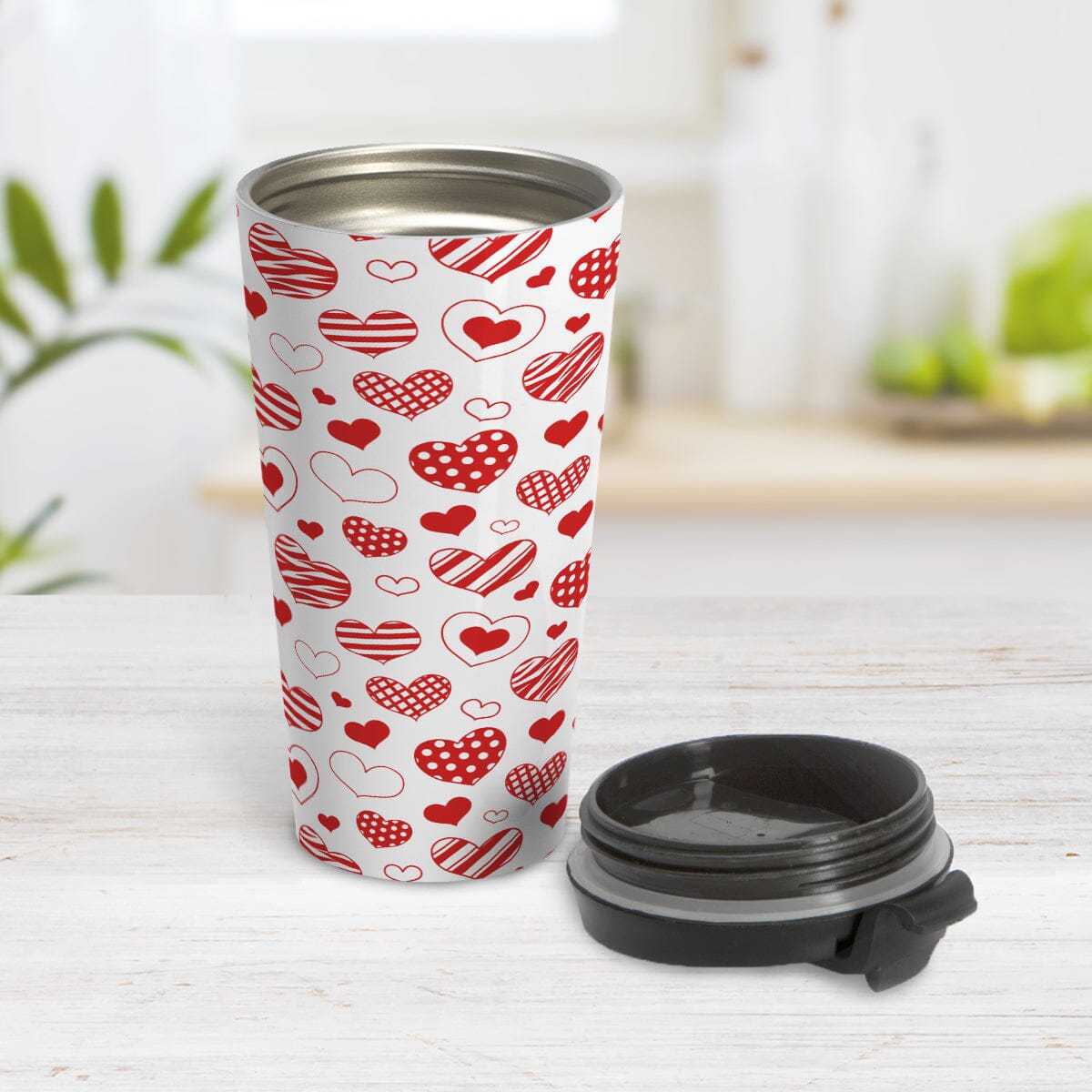 Red Heart Doodles Travel Mug (15oz) at Amy's Coffee Mugs. A stainless steel travel mug designed with hand-drawn red heart doodles in a pattern that wraps around the travel mug. This cute heart pattern is perfect for Valentine's Day or for anyone who loves hearts and young-at-heart drawings. Photo shows travel mug open with the lid on the table beside it.