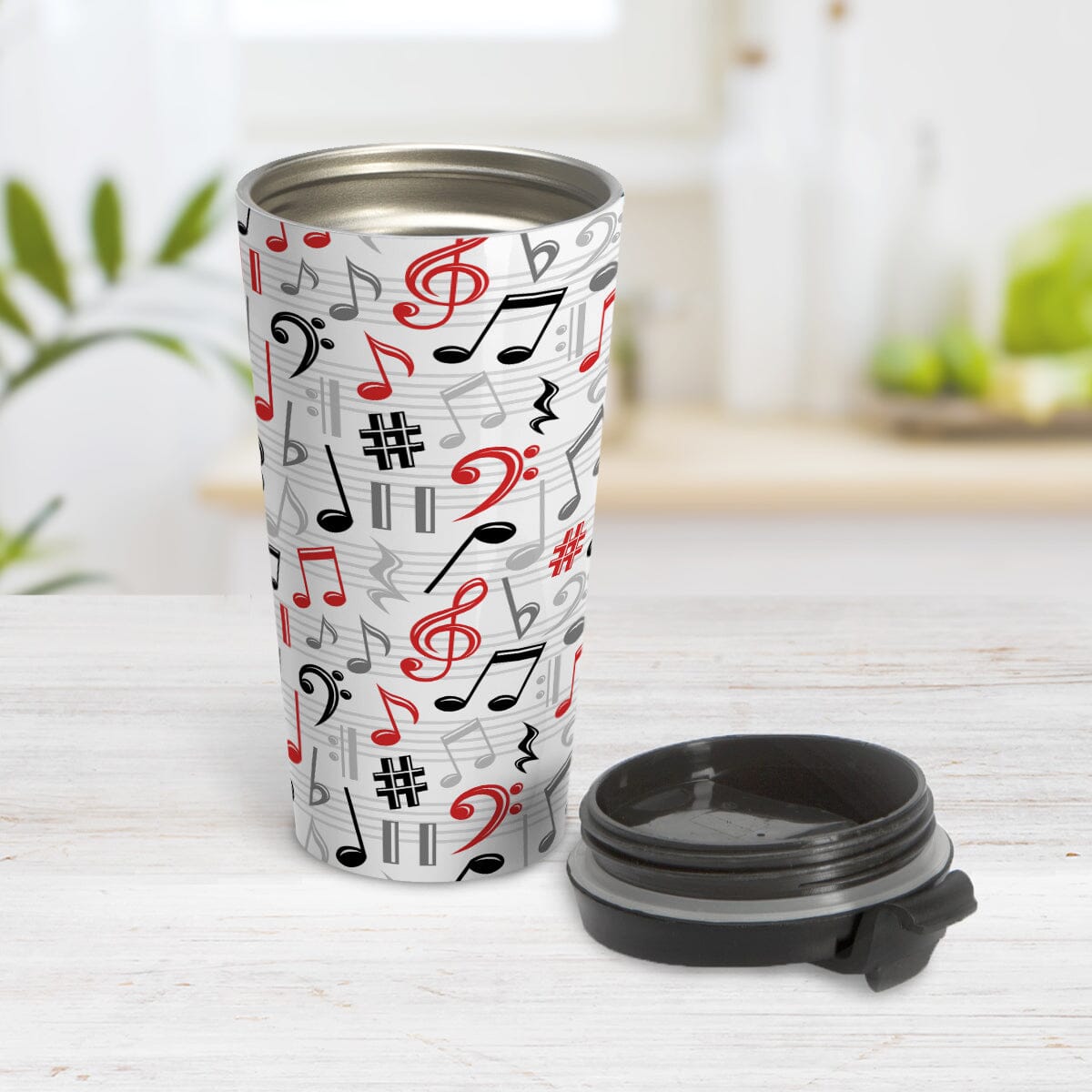 Red Music Notes Pattern Travel Mug (15oz) at Amy's Coffee Mugs. A stainless steel travel mug designed with music notes and symbols in red, black, and gray in a pattern that wraps around the travel mug. Photo shows the travel mug open with the lid laying on the tabletop beside it.