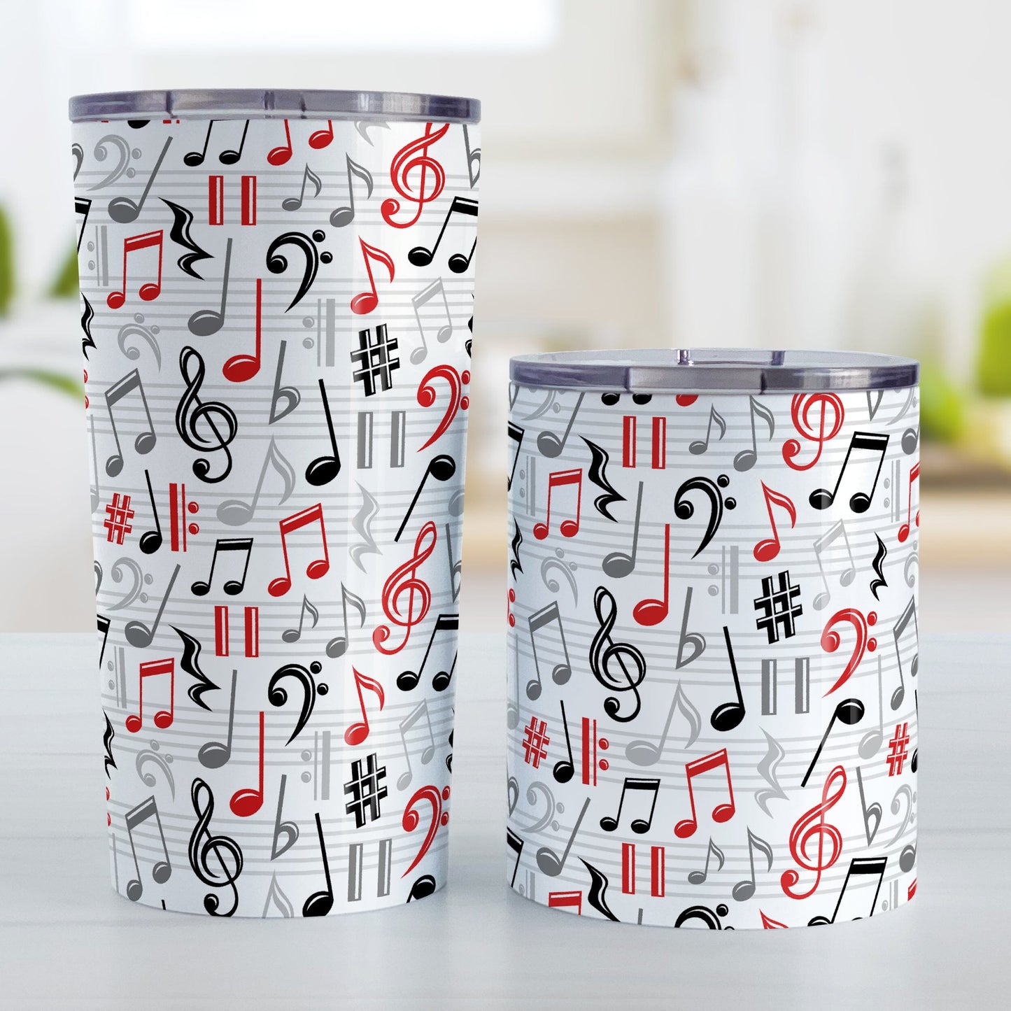 Red Music Notes Pattern Tumbler Cups (20oz or 10oz) at Amy's Coffee Mugs. Stainless steel tumbler cups designed with music notes and symbols in red, black, and gray in a pattern that wraps around the cups. Photo shows both cups on a table next to each other.