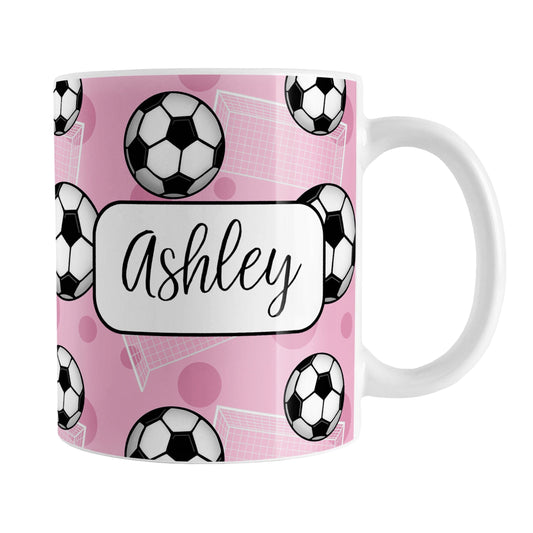 Soccer Ball and Goal Personalized Pink Soccer Mug (11oz) at Amy's Coffee Mugs. A ceramic coffee mug designed with a pattern of soccer balls and white soccer goals over a pink background with pink circles. Your personalized name is custom-printed in a fun black script font on both sides of the mug over the soccer pattern.