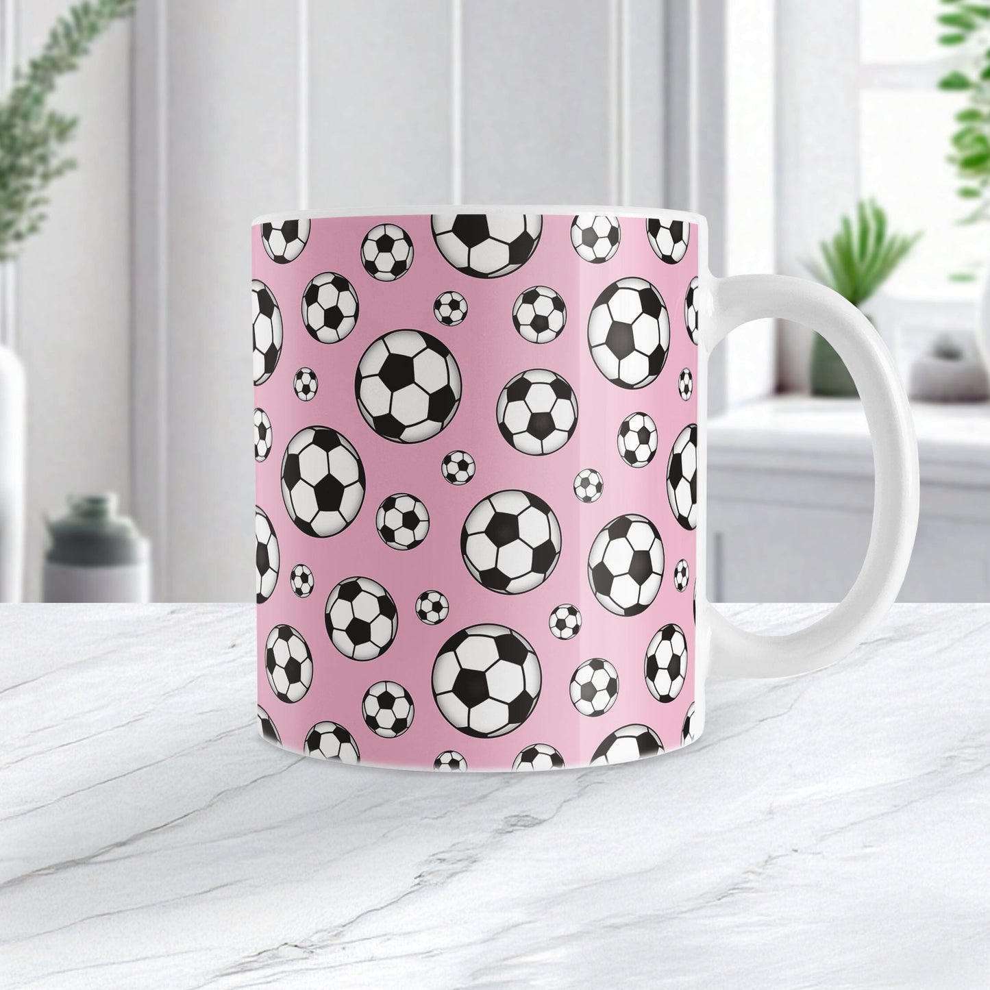 11oz white ceramic mug with a design of soccer balls over pink, on a marble countertop