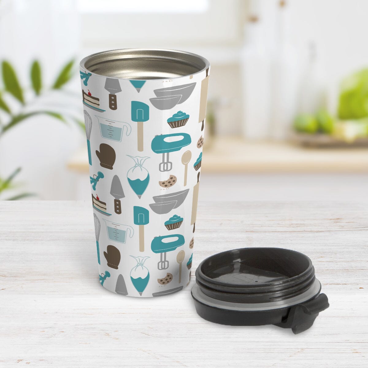Turquoise Baking Pattern Travel Mug (15oz) at Amy's Coffee Mugs. A stainless steel travel mug designed with a pattern of baking tools like spatulas, whisks, mixers, bowls, and spoons, with cookies, cupcakes, and cake all in a turquoise, gray, brown, and beige color scheme that wraps around the travel mug. Photo shows the travel mug open with the lid laying on the tabletop beside it.