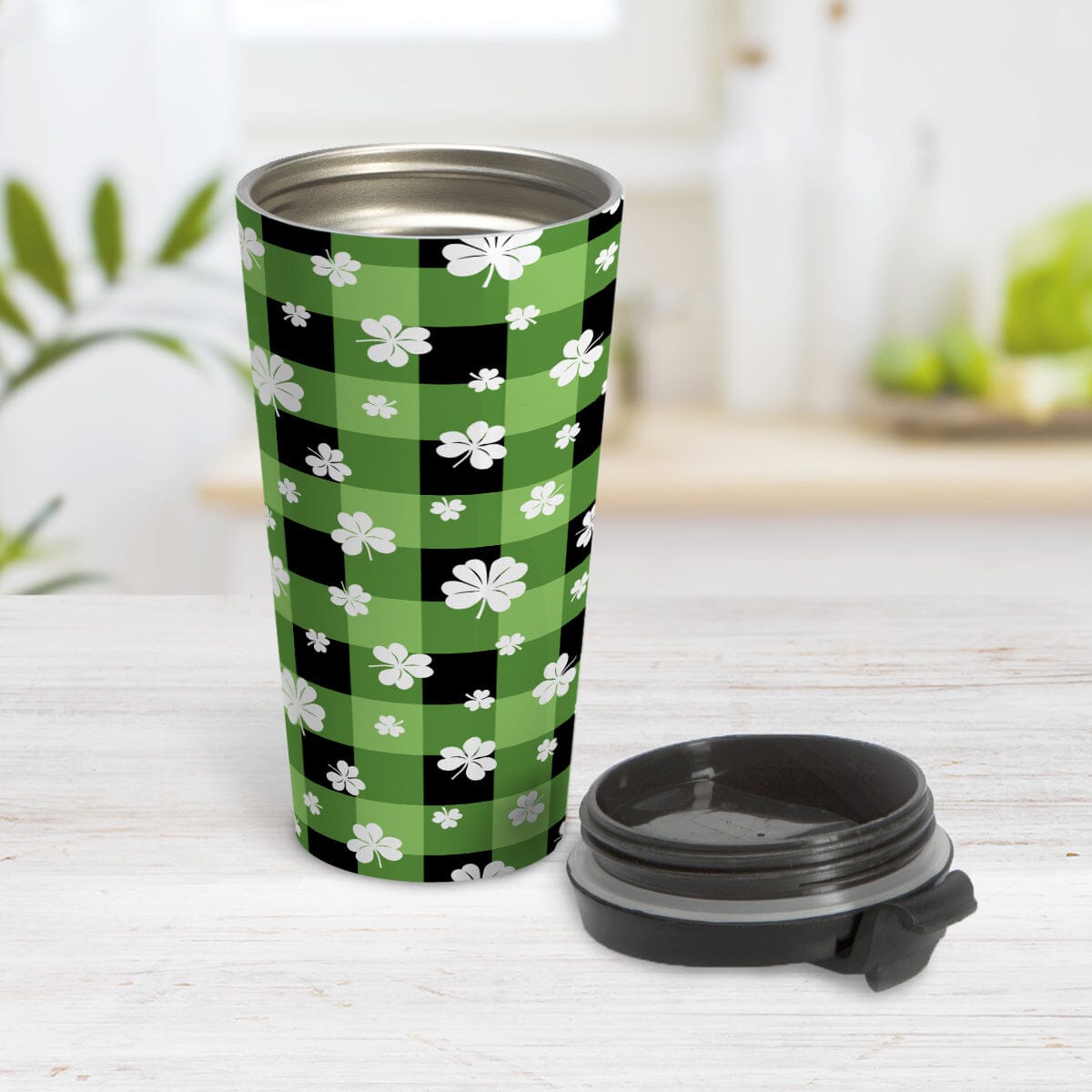 15oz travel mug with green and black checkered (buffalo plaid) pattern and white clovers, on a tabletop, open with the lid beside it