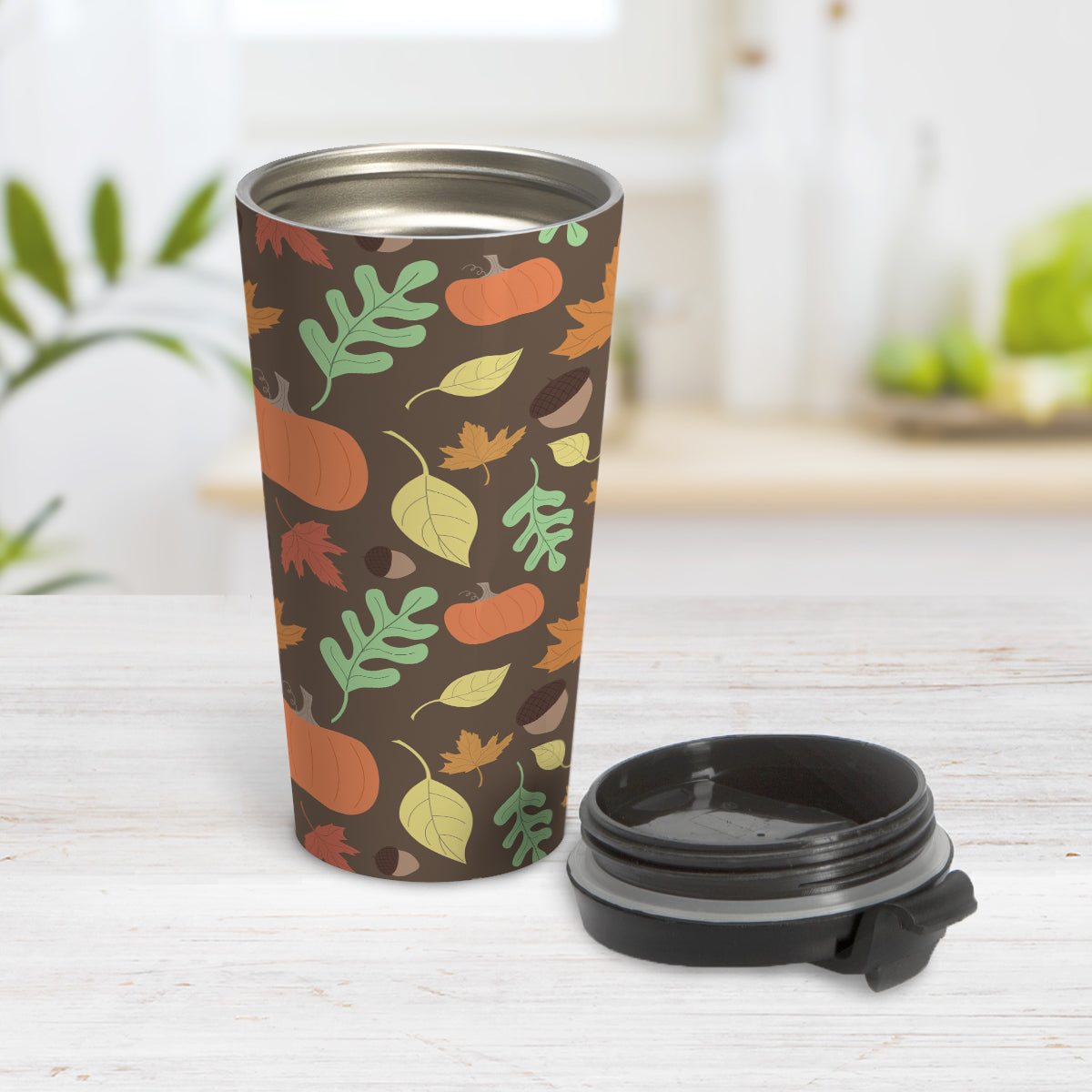 Autumn Pumpkins and Leaves Pattern - Fall Travel Mug (15oz) at Amy's Coffee Mugs. A travel mug designed with a pattern of pumpkins, acorns, and leaves in orange, yellow, and green over a brown background color that wraps around the travel mug. Photo shows the mug open on a table with the lid beside it.
