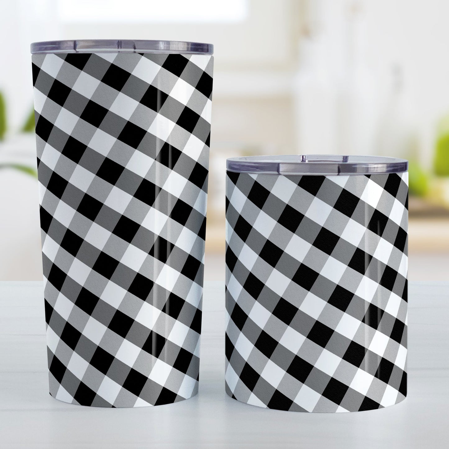 Black and White Gingham Tumbler Cup (20oz and 10oz, stainless steel insulated) at Amy's Coffee Mugs. Tumbler cups designed with a slanted black and white gingham pattern that wraps around the cups. Photo shows both sized cups on a table next to each other.