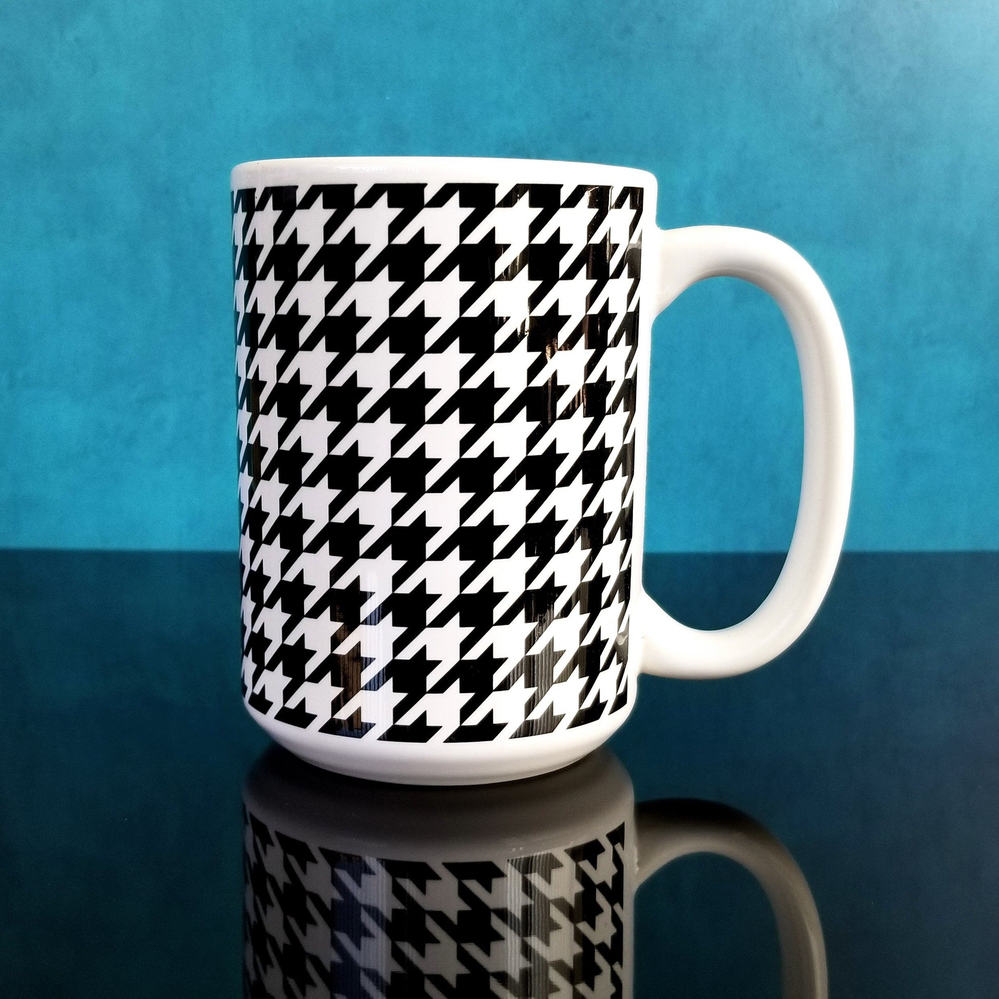 Black and White Houndstooth Mug (15oz, on blue and glossy black background) at Amy's Coffee Mugs. A ceramic coffee mug designed with a black and white houndstooth (dogtooth) pattern that wraps around the mug up to the handle.