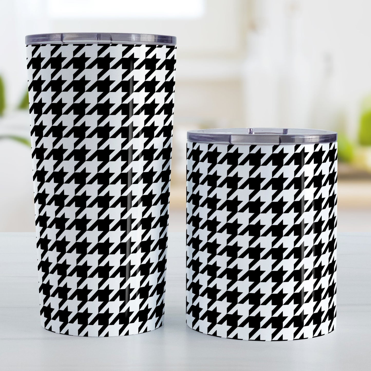 Black and White Houndstooth Tumbler Cup (20oz and 10oz, stainless steel insulated) at Amy's Coffee Mugs. Tumbler cups designed with a black and white houndstooth (dogtooth) pattern that wraps around the cups. Photo shows both sized cups on a table next to each other.