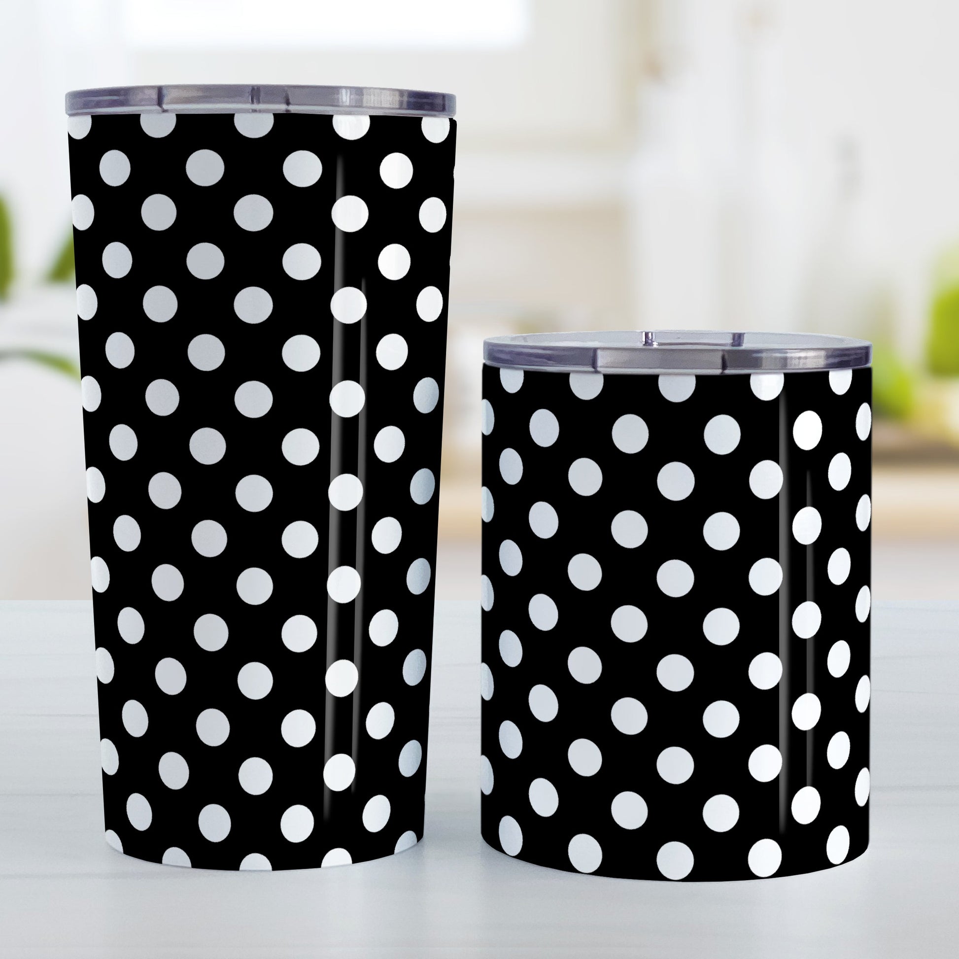 Black Polka Dot Tumbler Cup (20oz and 10oz, stainless steel insulated) at Amy's Coffee Mugs. Tumbler cups designed with a pattern of white polka dots over a black background color that wraps around the cups. Photo shows both sized cups on a table next to each other.