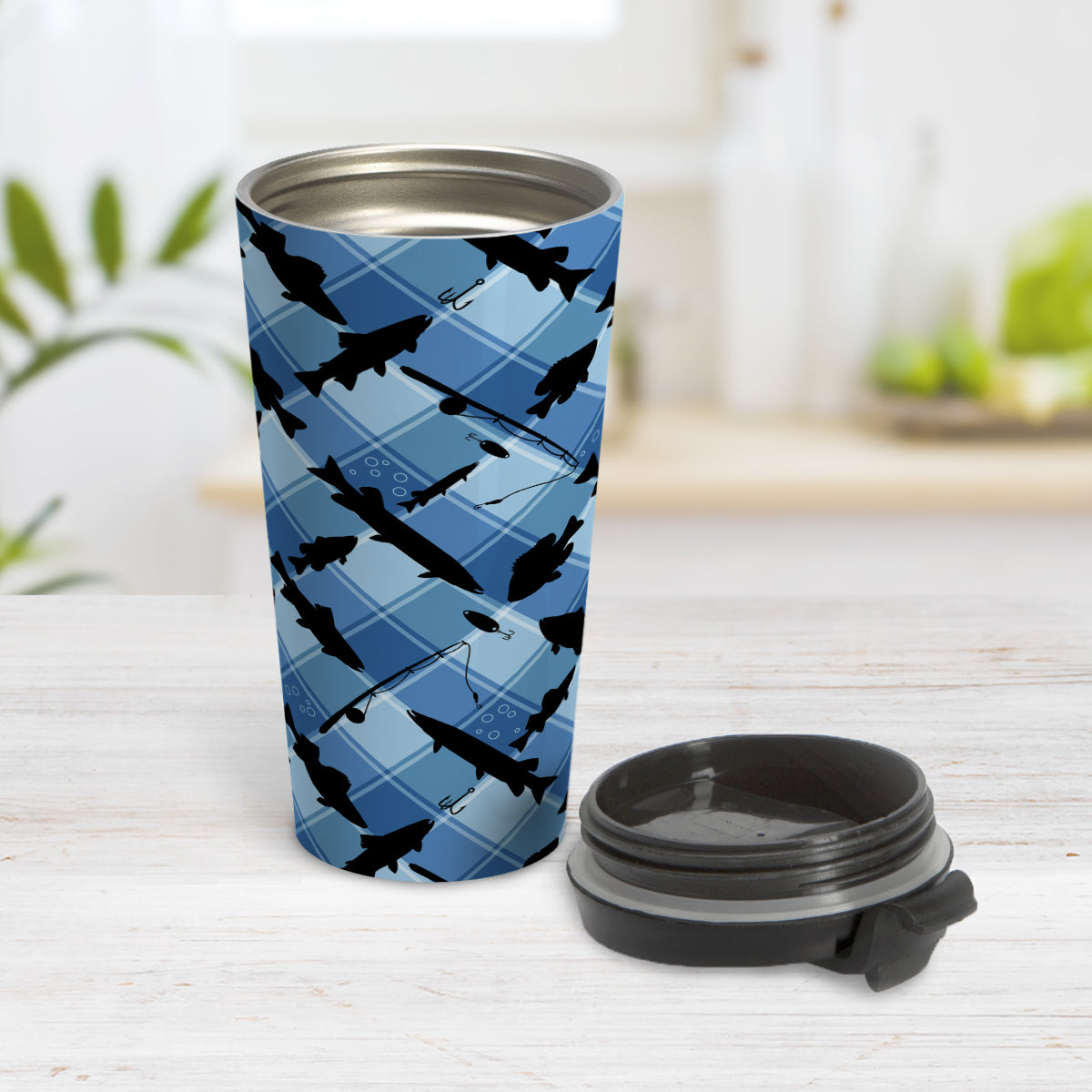 Blue Fishing Plaid Pattern Travel Mug (15oz) at Amy's Coffee Mugs. A travel mug designed with black silhouettes of fish, fishing poles, and lures diagonally arranged over a blue plaid pattern that wraps around the travel mug. Photo shows the mug open on a table with the lid beside it.