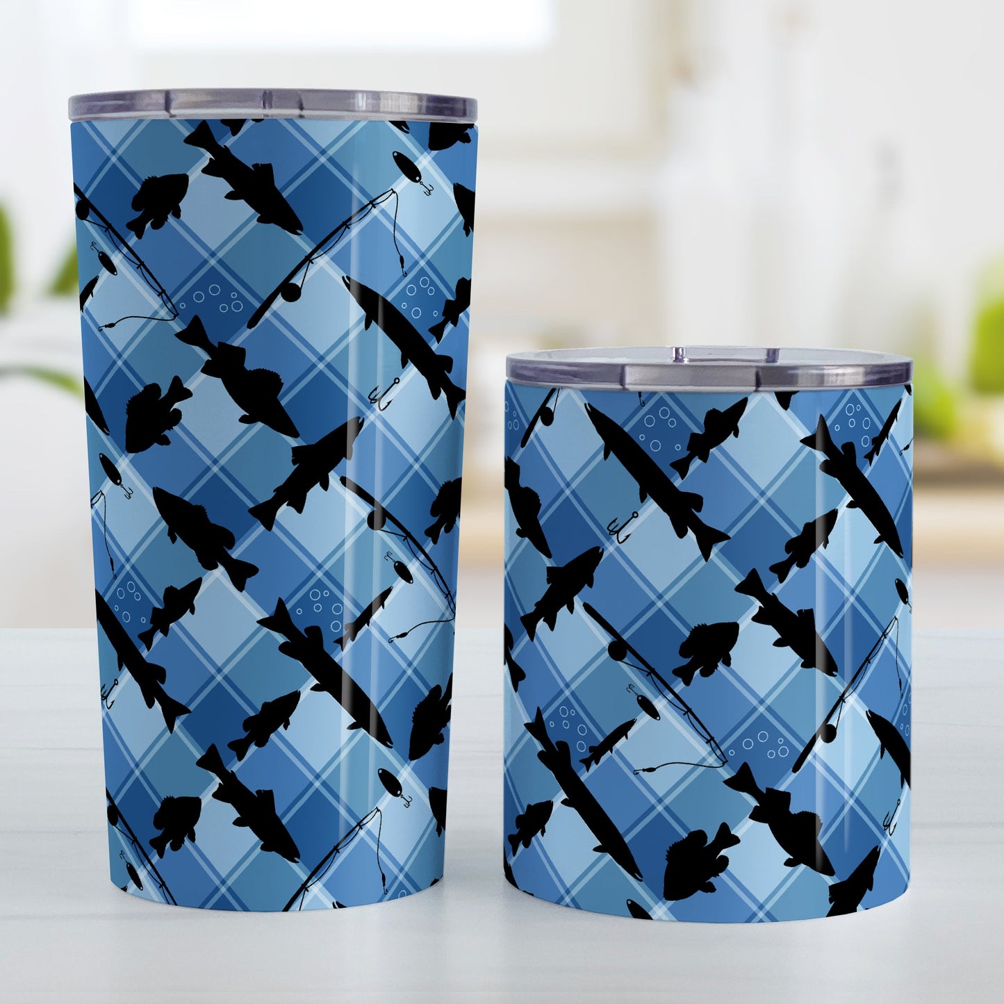 Blue Fishing Plaid Pattern Tumbler Cup (20oz and 10oz, stainless steel insulated) at Amy's Coffee Mugs. Tumbler cups designed with black silhouettes of fish, fishing poles, and lures diagonally arranged over a blue plaid pattern that wraps around the cups. Photo shows both sized cups on a table next to each other.