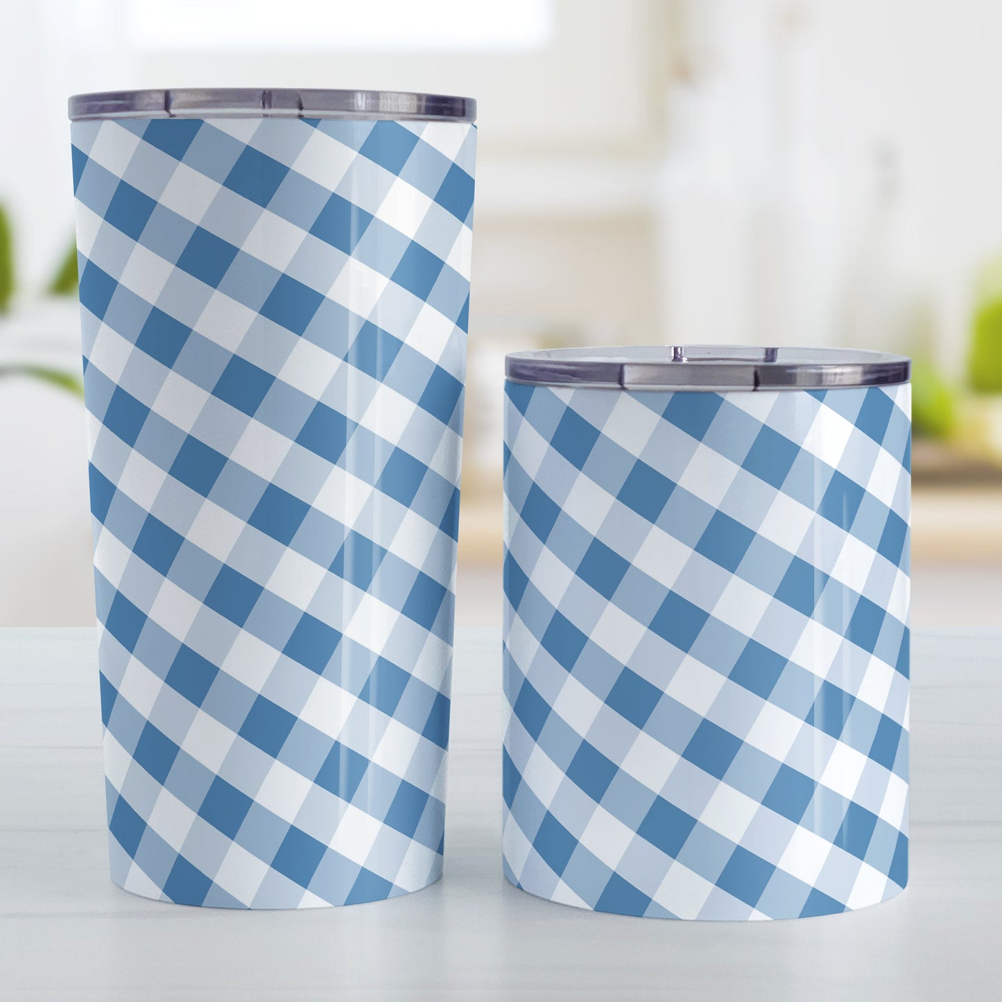 Blue Gingham Tumbler Cup (20oz and 10oz, stainless steel insulated) at Amy's Coffee Mugs. Tumbler cups designed with a slanted blue and white gingham pattern that wraps around the cups. Photo shows both sized cups on a table next to each other.