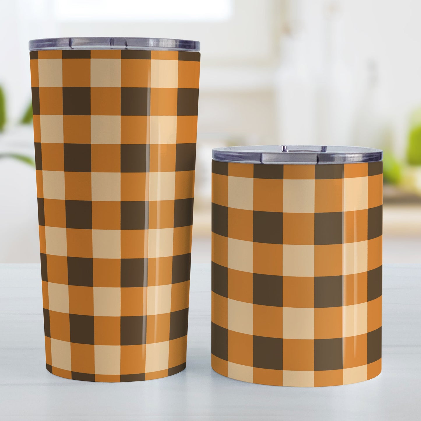 Brown and Orange Fall Buffalo Plaid Tumbler Cup (20oz and 10oz, stainless steel insulated) at Amy's Coffee Mugs. Tumbler cups designed with a fall-inspired buffalo plaid (buffalo check) pattern in brown, orange, and beige. This pattern wraps around the cups. Photo shows both sized cups on a table next to each other.