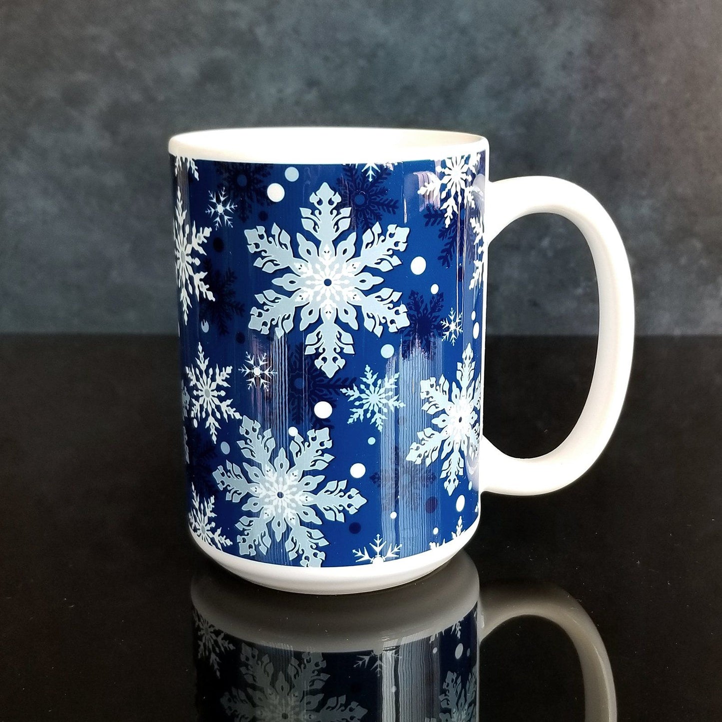 Classic Blue Snowflake Pattern Winter Mug (15oz) on glassy black and midnight background. A ceramic coffee mug designed with a pattern of different shades of blue snowflakes over a classic blue background color that wraps around the mug.