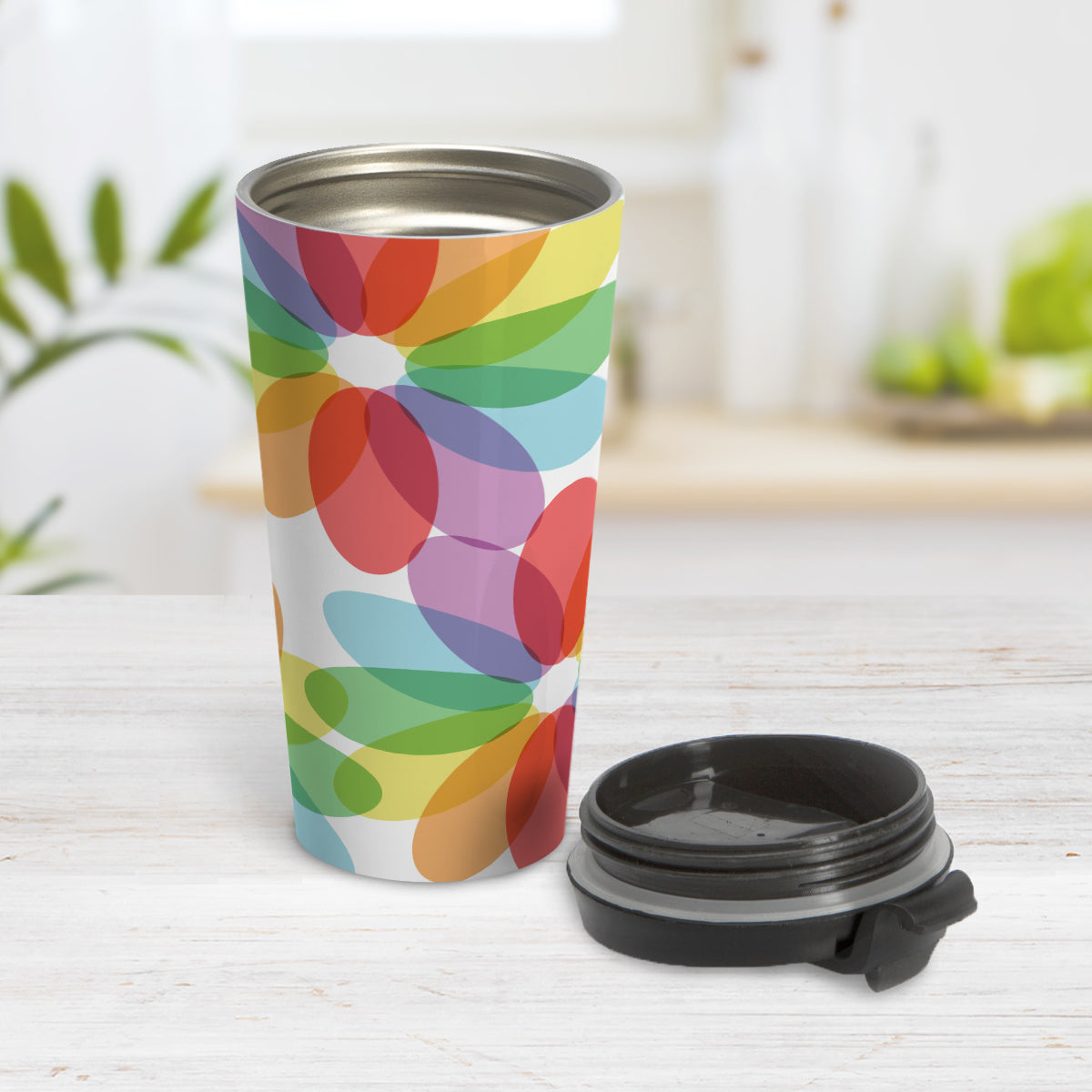 Color Lovers Rainbow Flower Travel Mug (15oz) at Amy's Coffee Mugs. A travel mug with large colorful flower-like designs with each oval petal presenting a different progression in the rainbow, blending into each other, in a pattern that wraps around the travel mug. Photo shows the mug open on a table with the lid beside it.
