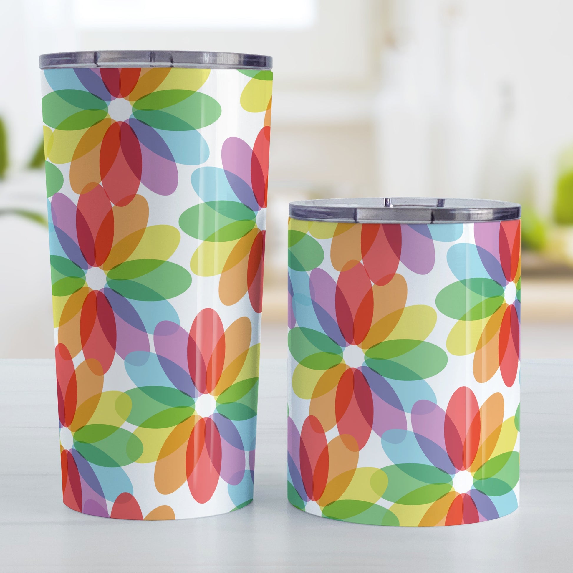 Color Lovers Rainbow Flower Tumbler Cup (20oz and 10oz, stainless steel insulated) at Amy's Coffee Mugs. Tumbler cups with large colorful flower-like designs with each oval petal presenting a different progression in the rainbow, blending into each other, in a pattern that wraps around the cups. Photo shows both sized cups on a table next to each other.