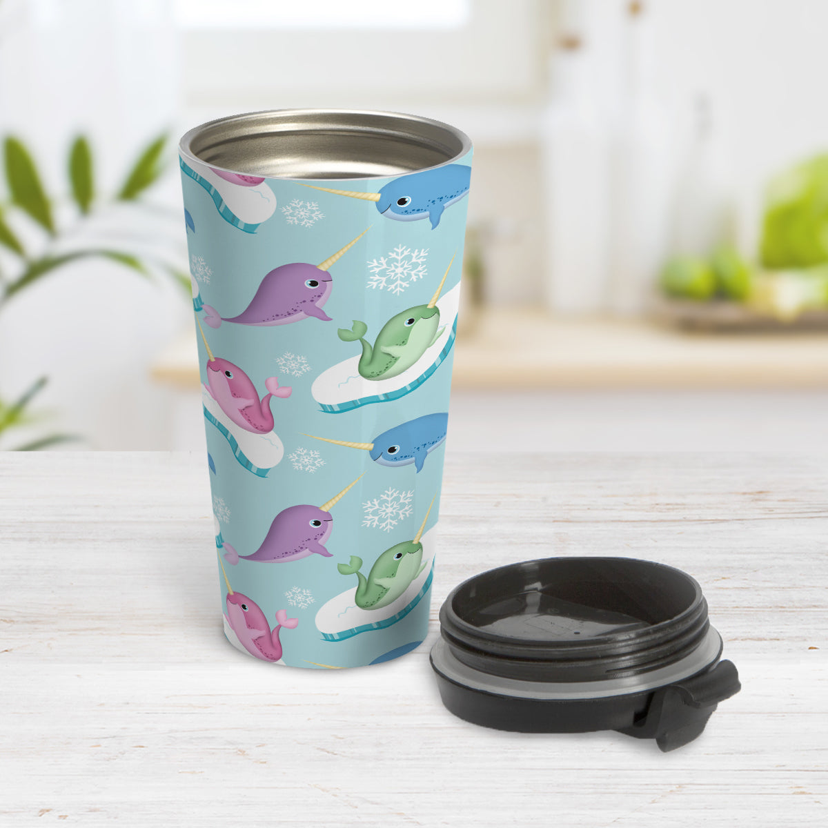 Colorful Arctic Narwhal Pattern Travel Mug (15oz) at Amy's Coffee Mugs. A travel mug designed cute pink, purple, blue, and green narwhals with icebergs and snowflakes over a light blue colored background that wraps around the travel mug. Photo shows the mug open on a table with its lid next to it.