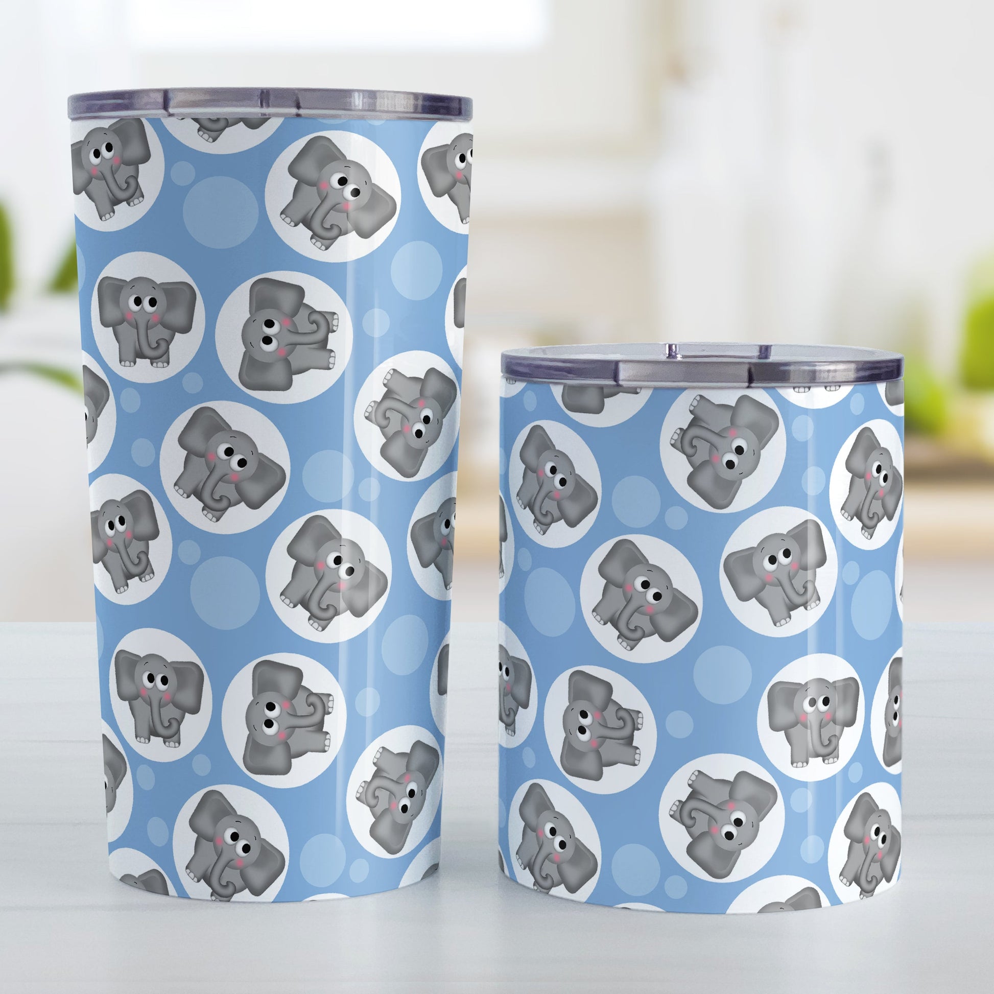 Cute Blue Elephant Pattern Tumbler Cup (20oz and 10oz, stainless steel insulated) at Amy's Coffee Mugs. Tumbler cups designed with cute and affectionate gray elephants in white circles scattered over a blue background color in a pattern that wraps around the cups. Photo shows both sized cups on a table next to each other.