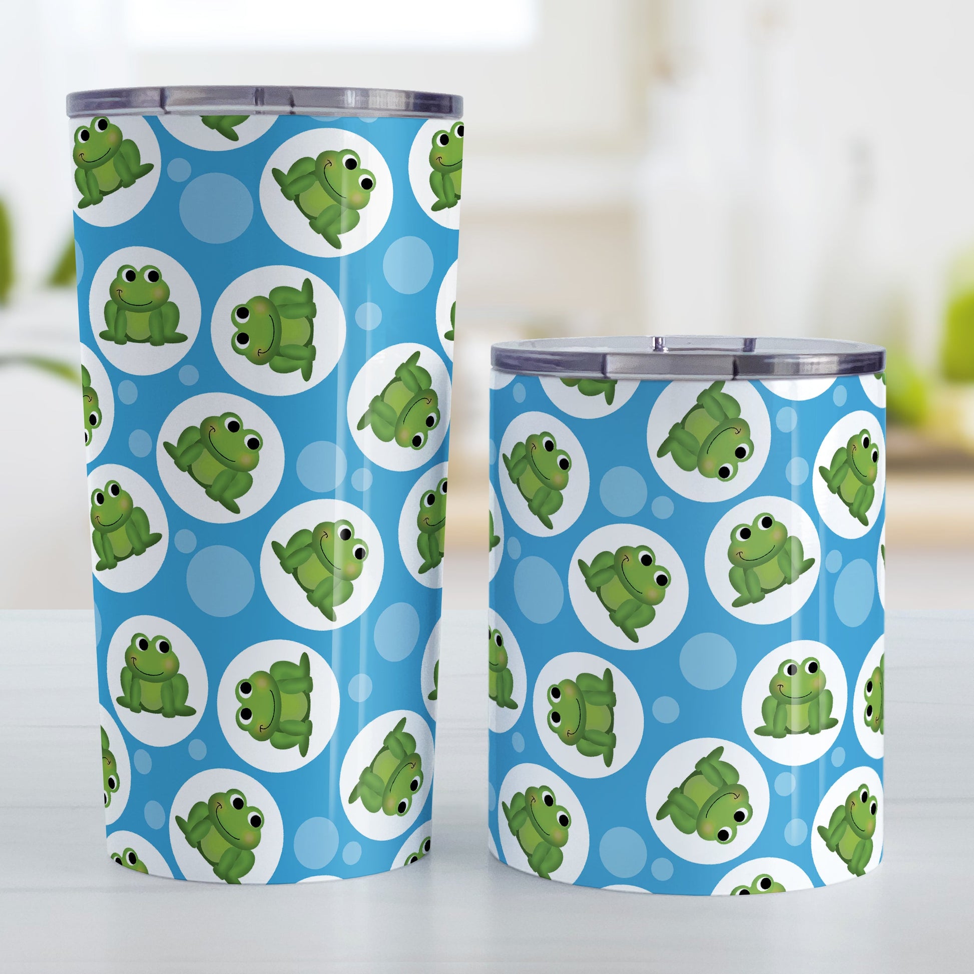 Cute Blue Frog Pattern Tumbler Cup (20oz and 10oz, stainless steel insulated) at Amy's Coffee Mugs. Tumbler cups designed with cute and smiling green frogs in white circles scattered over a blue background color in a pattern that wraps around the cups. Photo shows both sized cups on a table next to each other.