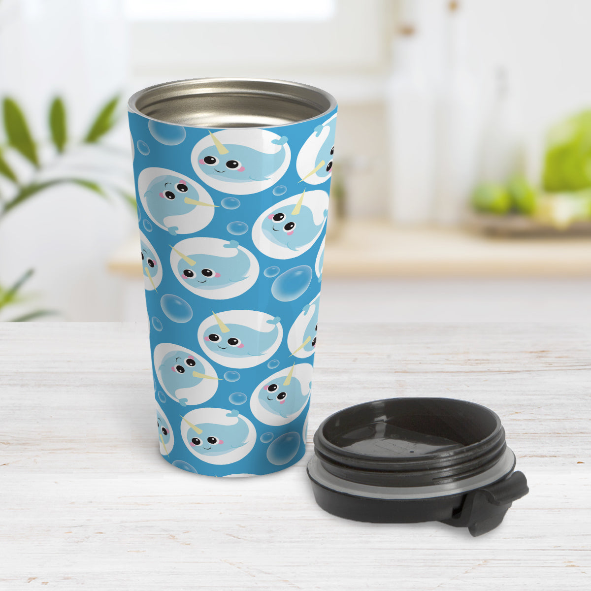 Cute Blue Narwhal Bubble Pattern Travel Mug (15oz) at Amy's Coffee Mugs. A travel mug designed with cute light blue narwhals in white circles and with bubbles scattered over a blue background color in a pattern that wraps around the travel mug. Photo shows the mug open on a table with its lid next to it.