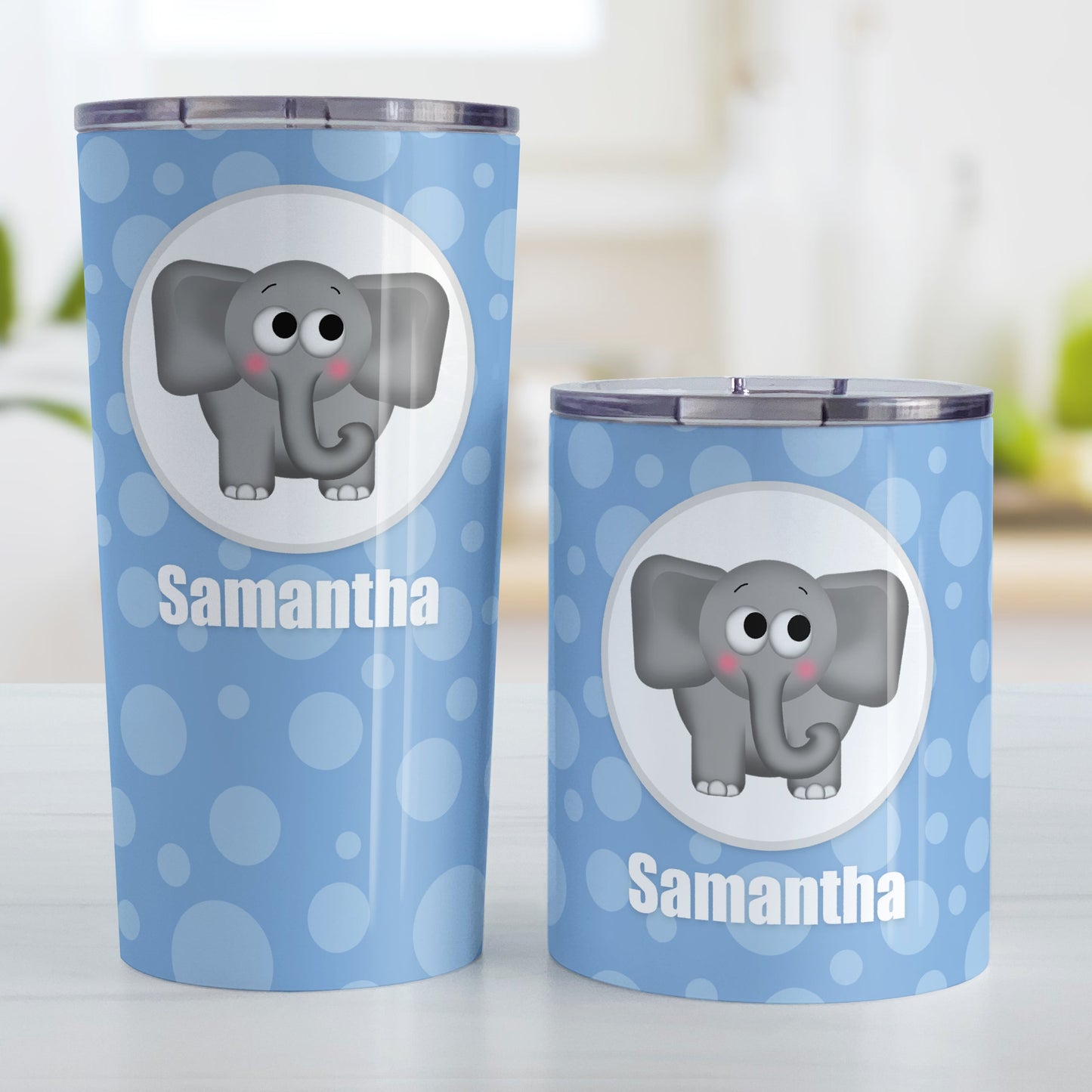 Cute Elephant Bubbly Blue Personalized Tumbler Cup (20oz and 10oz, stainless steel insulated) at Amy's Coffee Mugs. A tumbler cup designed with an adorable and affectionate gray elephant in a white circle outlined in gray over a blue bubbly background that wraps around the cup. Your name is personalized in white below the cute elephant. Photo shows both sized cups on a table next to each other.