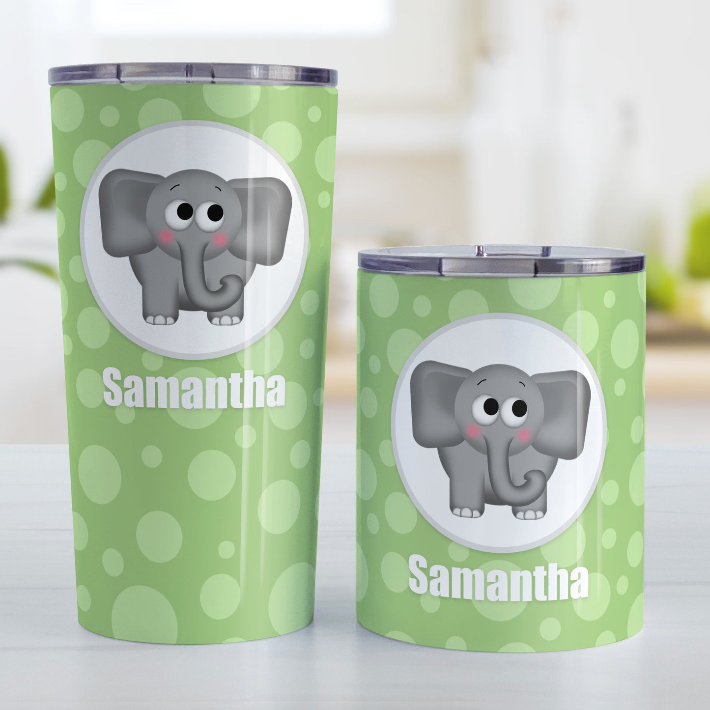 Cute Elephant Bubbly Green Personalized Tumbler Cup (20oz and 10oz, stainless steel insulated) at Amy's Coffee Mugs. A tumbler cup designed with an adorable and affectionate gray elephant in a white circle outlined in gray over a green bubbly background that wraps around the cup. Your name is personalized in white below the cute elephant. Photo shows both sized cups on a table next to each other.