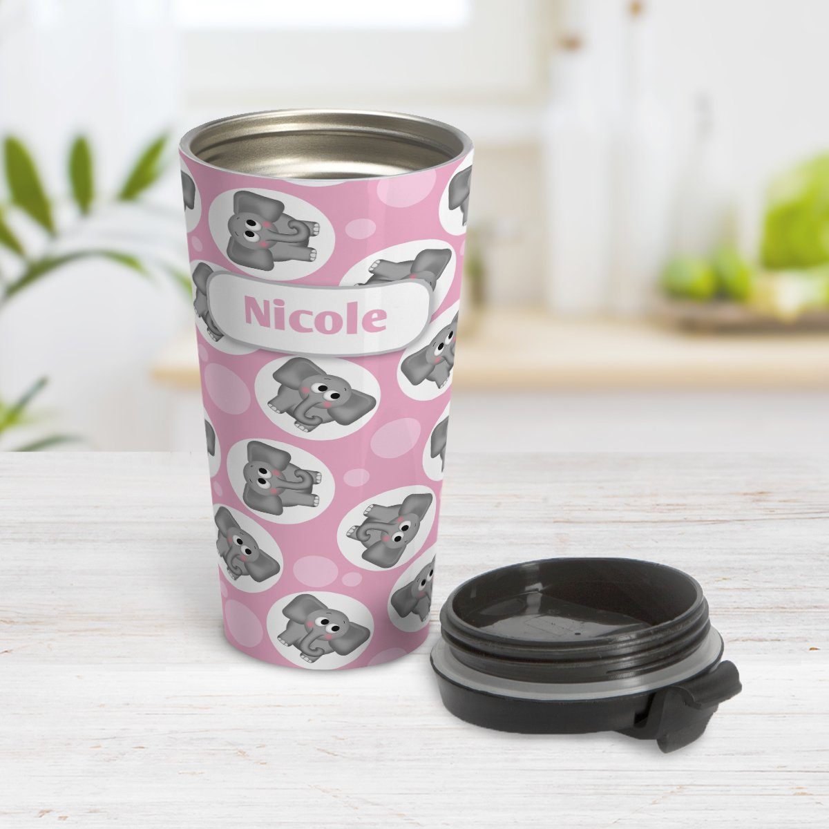 Cute Elephant Pattern - Personalized Pink Elephant Travel Mug at Amy's Coffee Mugs. A travel mug designed with cute and affectionate gray elephants in white circles scattered over a pink background color in a pattern that wraps around the travel mug. Your name is custom printed in pink on white positioned prominently over the elephant pattern. Photo shows the mug open on a table with its lid beside it.