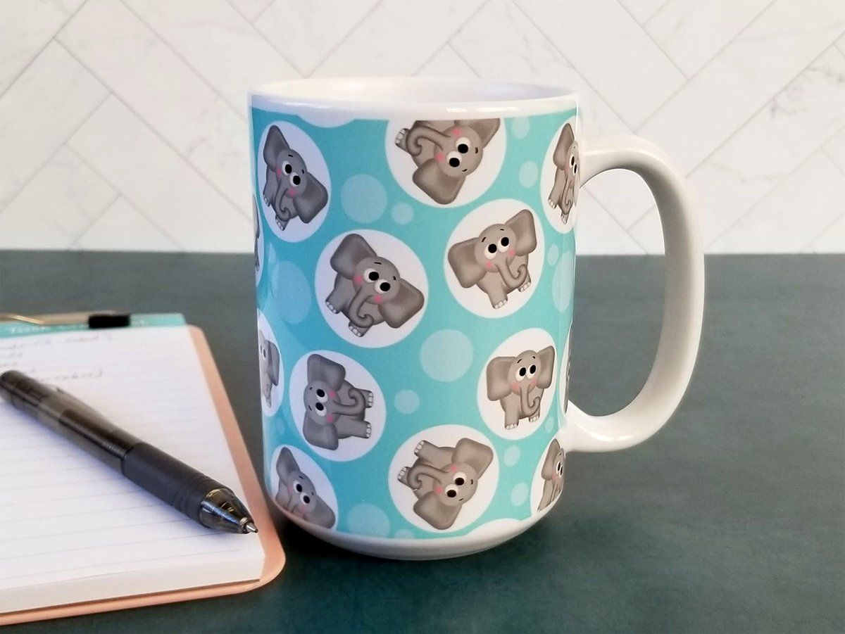 Cute Elephant Pattern - Turquoise Elephant Mug at Amy's Coffee Mugs. A ceramic coffee mug designed with cute and affectionate gray elephants in white circles scattered over a turquoise background color in a pattern that wraps around the mug up to the handle. Photo shows the mug on a table next to a notepad and pen.