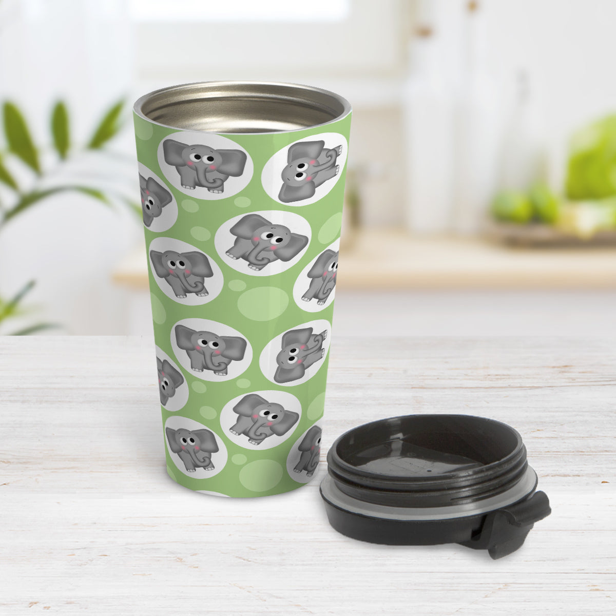 Cute Green Elephant Pattern Travel Mug (15oz) at Amy's Coffee Mugs. A travel mug designed with cute and affectionate gray elephants in white circles scattered over a green background color in a pattern that wraps around the travel mug. Photo shows the mug open on a table with its lid beside it.