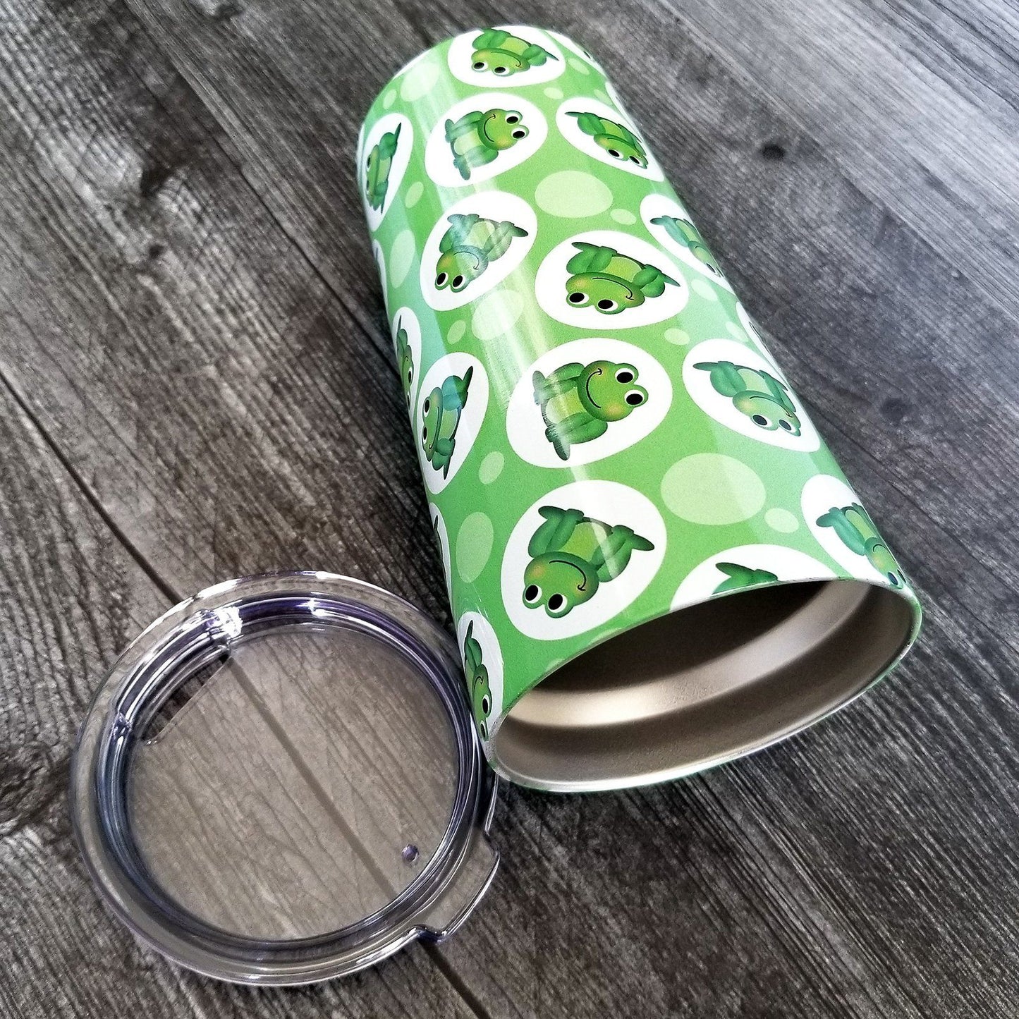 Cute Green Frog Pattern Tumbler Cup (20oz, on weathered wood) at Amy's Coffee Mugs. A tumbler cup designed with cute and smiling green frogs in white circles scattered over a green background color in a pattern that wraps around the cup.