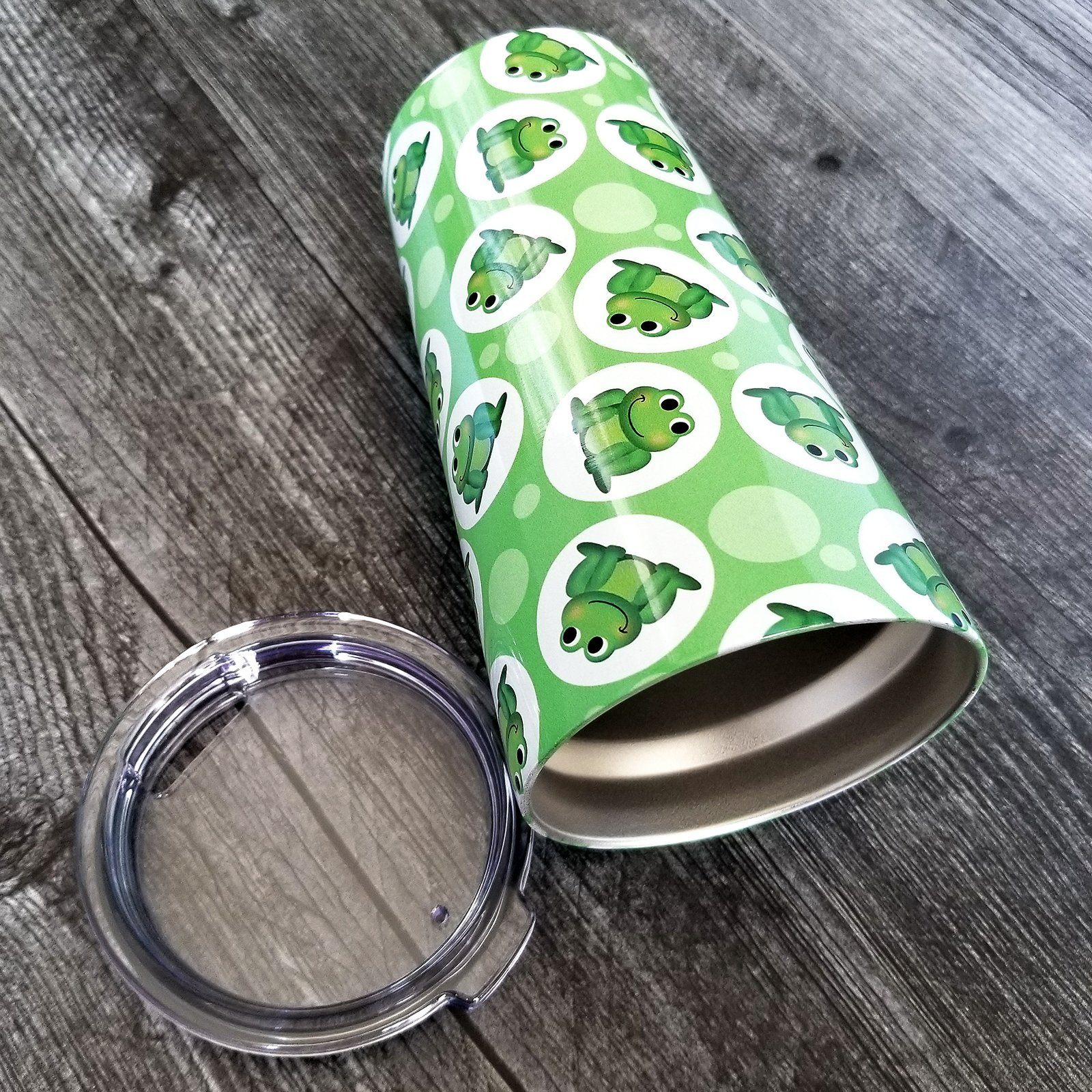 Cute Green Frog Pattern Tumbler Cup (20oz, on weathered wood) at Amy's Coffee Mugs. A tumbler cup designed with cute and smiling green frogs in white circles scattered over a green background color in a pattern that wraps around the cup.