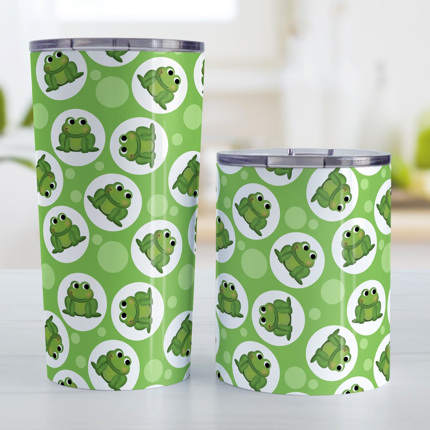 Cute Green Frog Pattern Tumbler Cup (20oz and 10oz, stainless steel insulated) at Amy's Coffee Mugs. Tumbler cups designed with cute and smiling green frogs in white circles scattered over a green background color in a pattern that wraps around the cups. Photo shows both sized cups on a table next to each other.